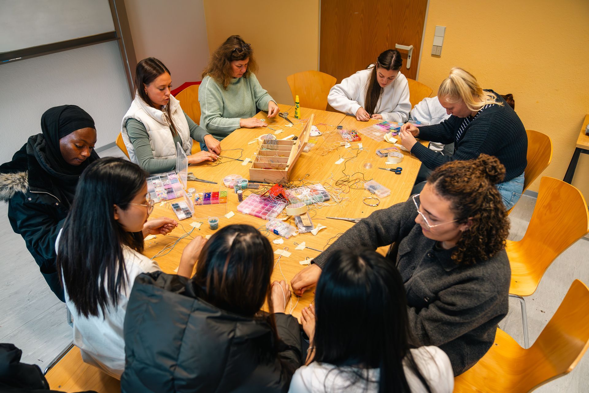 Menschen sitzen um einen Tisch und basteln gemeinsam. Holztisch und -stühle. Gut beleuchteter Raum.