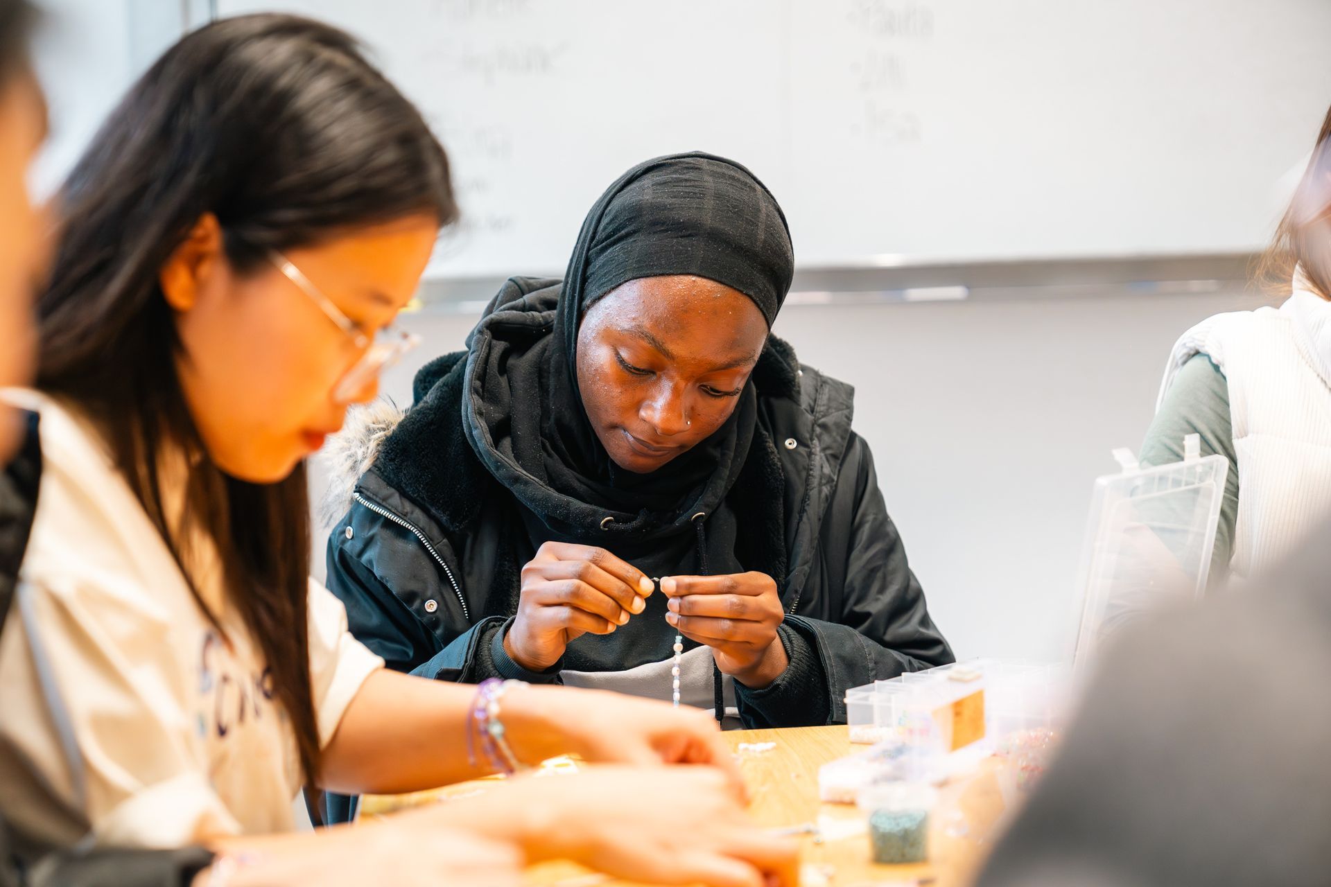 Menschen basteln an einem Tisch. Eine Person mit schwarzer Kopfbedeckung konzentriert sich auf ihre Hände. Weitere Personen sind um den Tisch herum zu sehen.