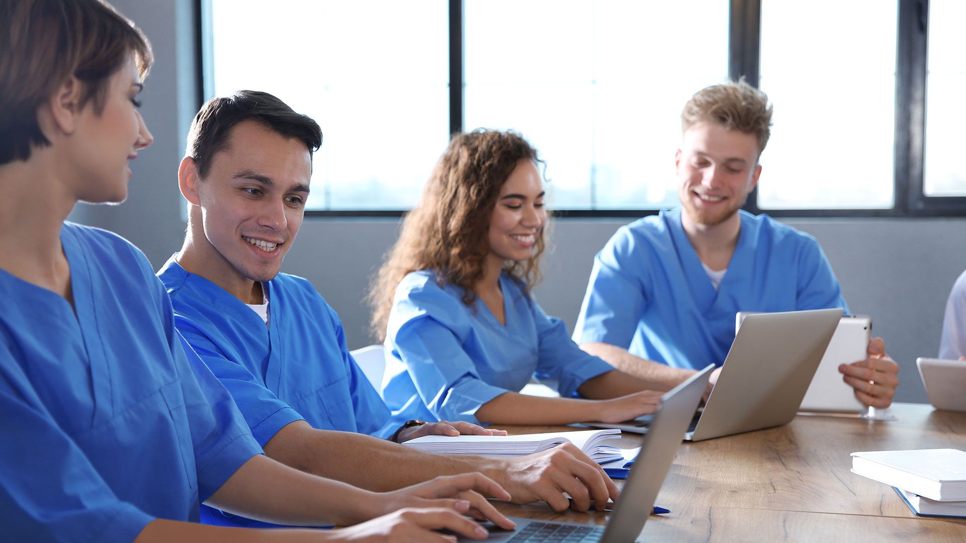 Eine Gruppe von Krankenpflegern sitzt an einem Tisch und benutzt Laptops