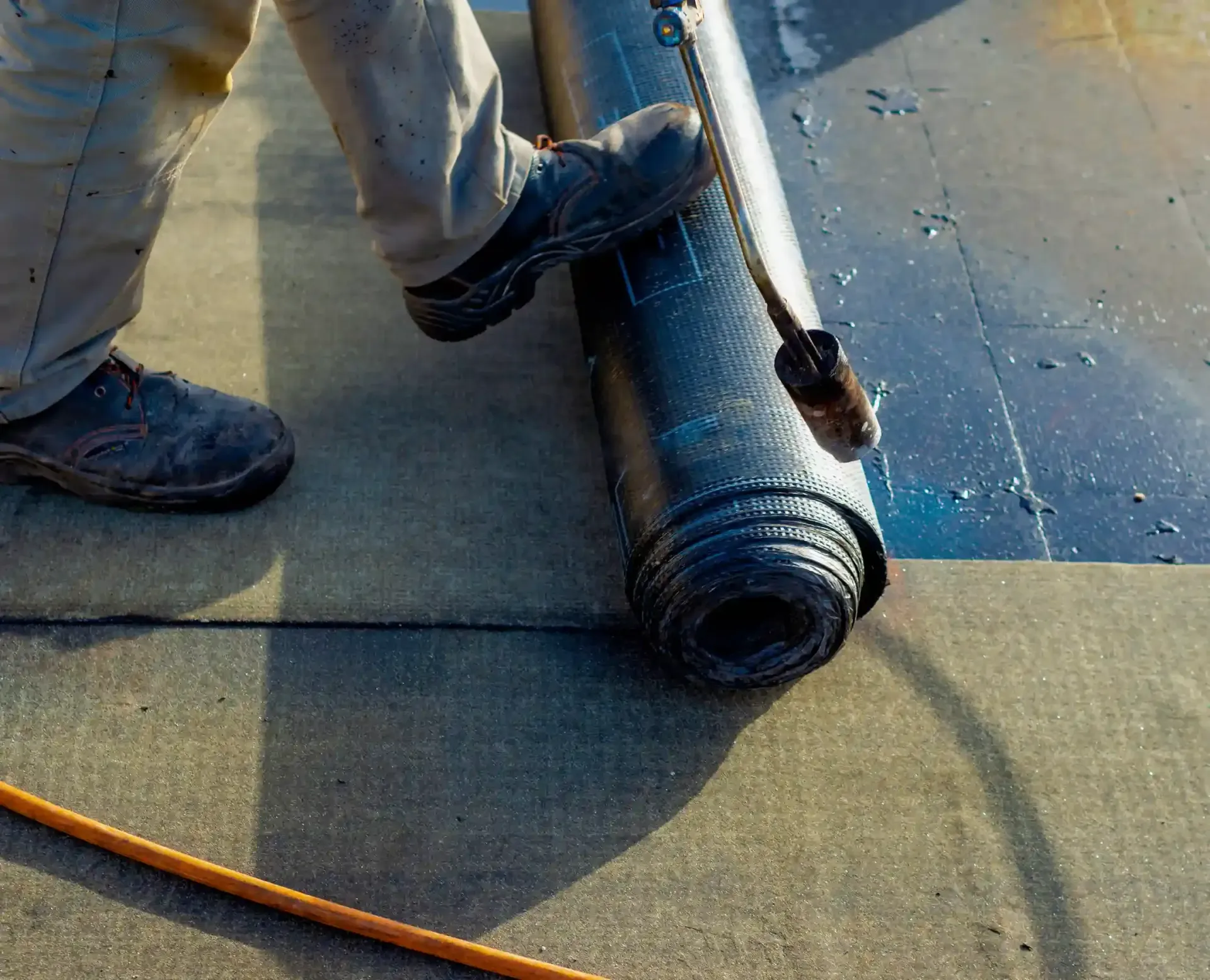 Persona extendiendo material para techos sobre un techo plano, usando un soplete.