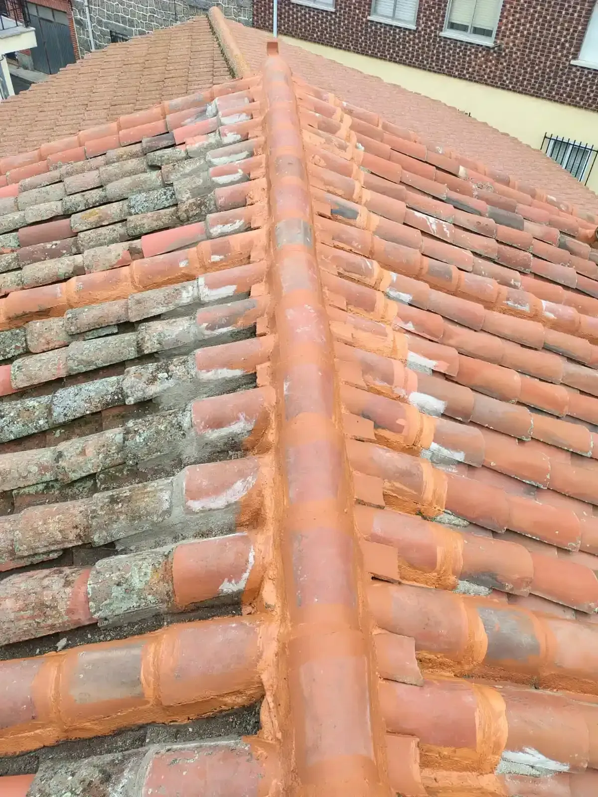 Techo de tejas rojas con cumbrera central, que muestra tejas desgastadas y un sellador.