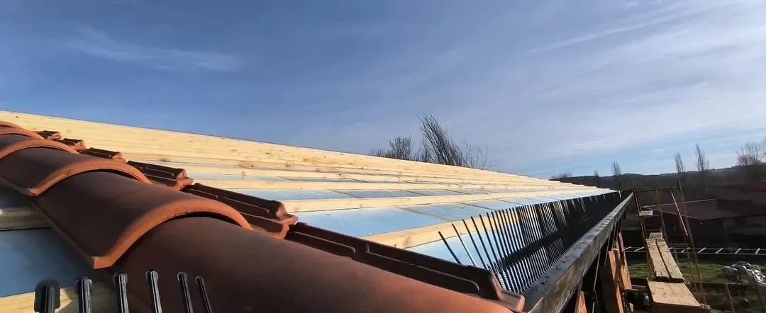 Techo en proceso con tejas de terracota, aislamiento azul y canalón metálico bajo un cielo azul.