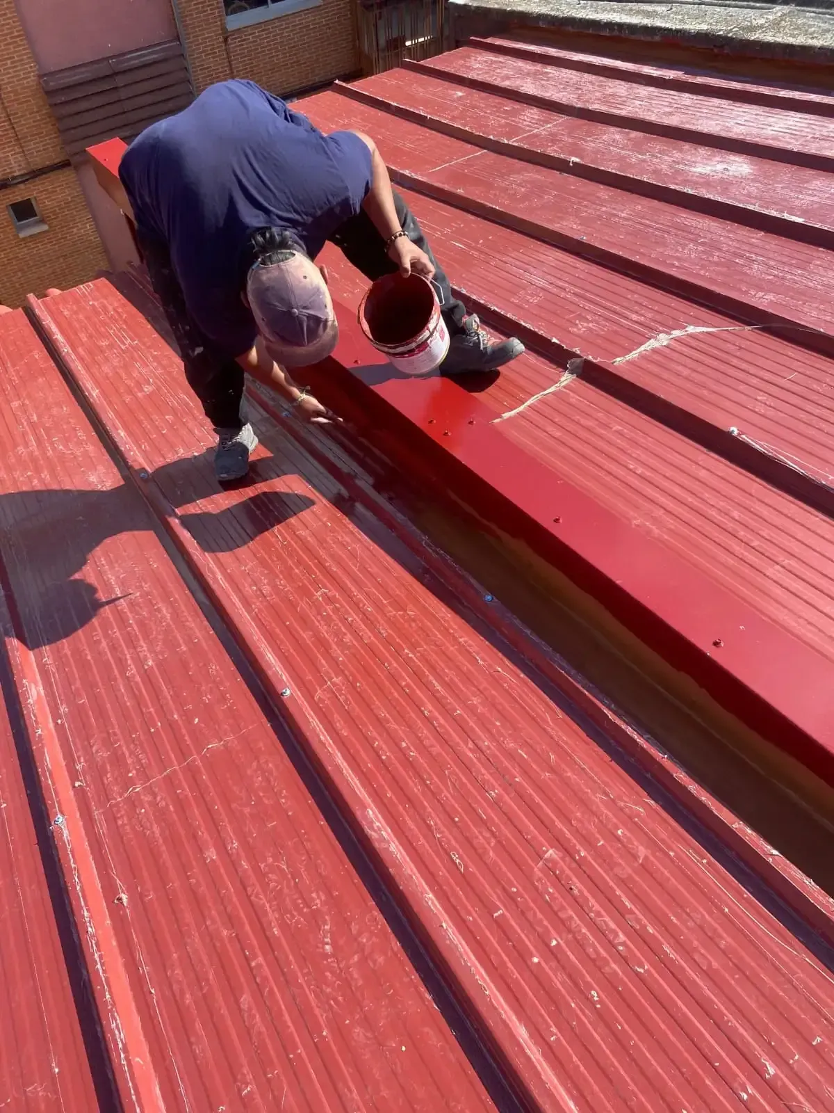 Una persona pinta un techo de metal rojo con un balde.