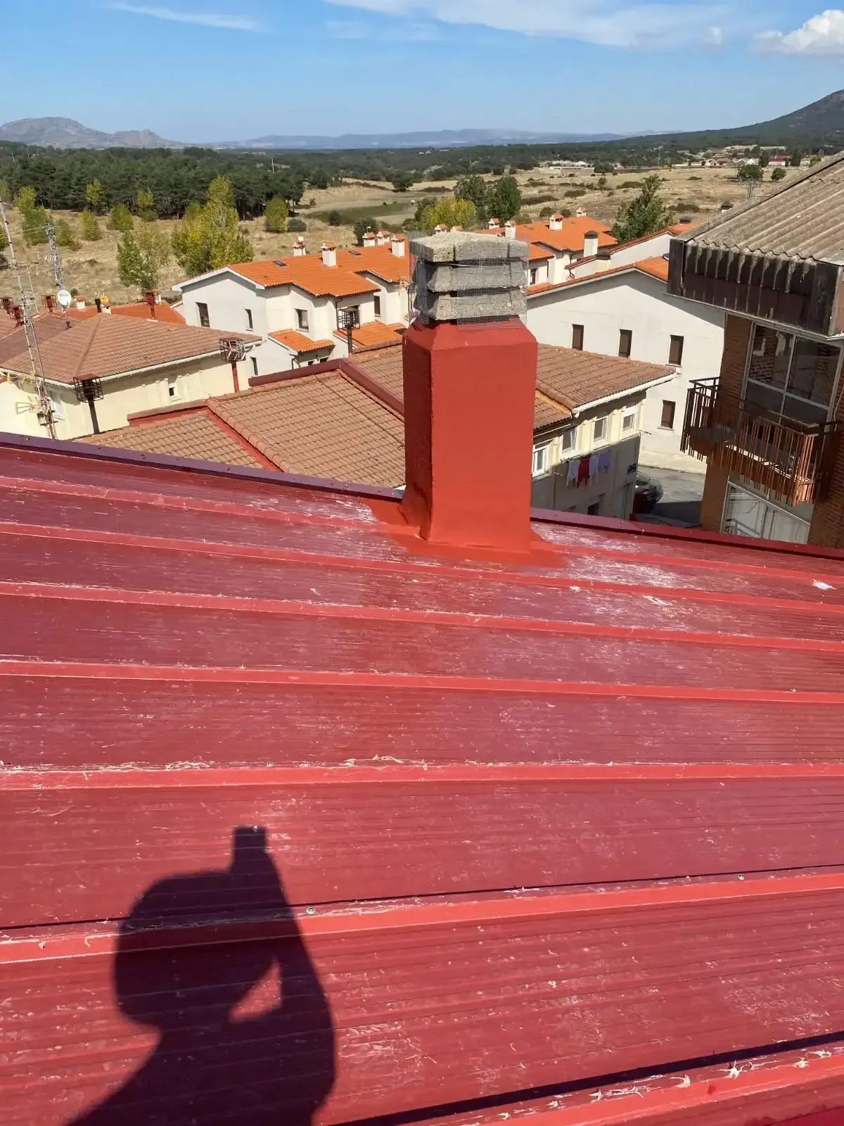 Techo de metal rojo con chimenea roja y fondo de paisaje urbano.