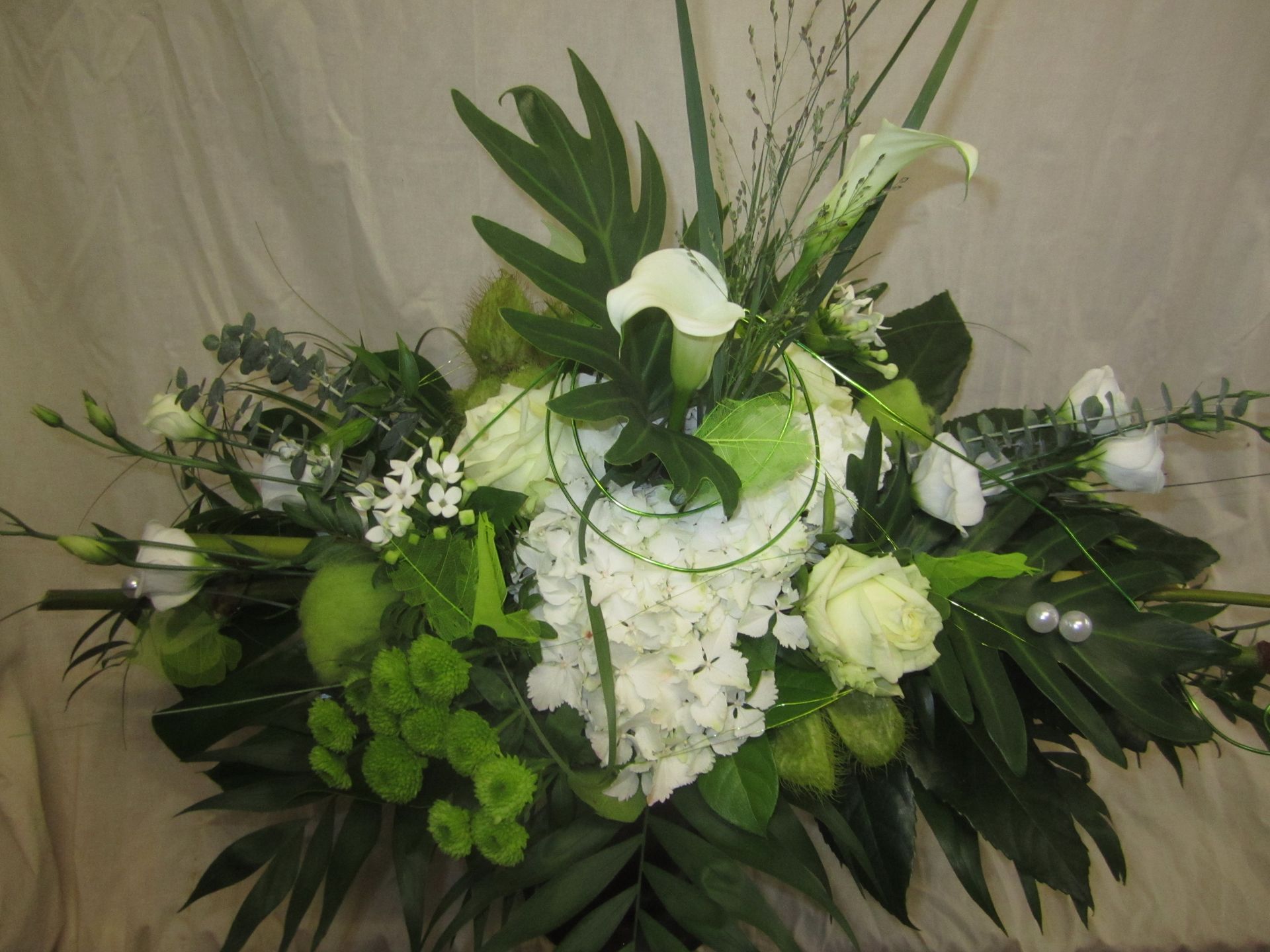 Blumenarrangement: weiße Hortensien, Callas, grüne Äpfel, Blätter und einige Perlen auf cremefarbenem Hintergrund.