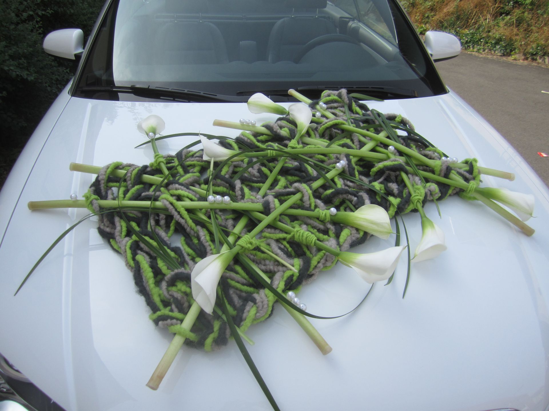 Weiße Motorhaube mit einem Blumenarrangement aus Calla-Lilien, grünem und schwarzem Strickmaterial.