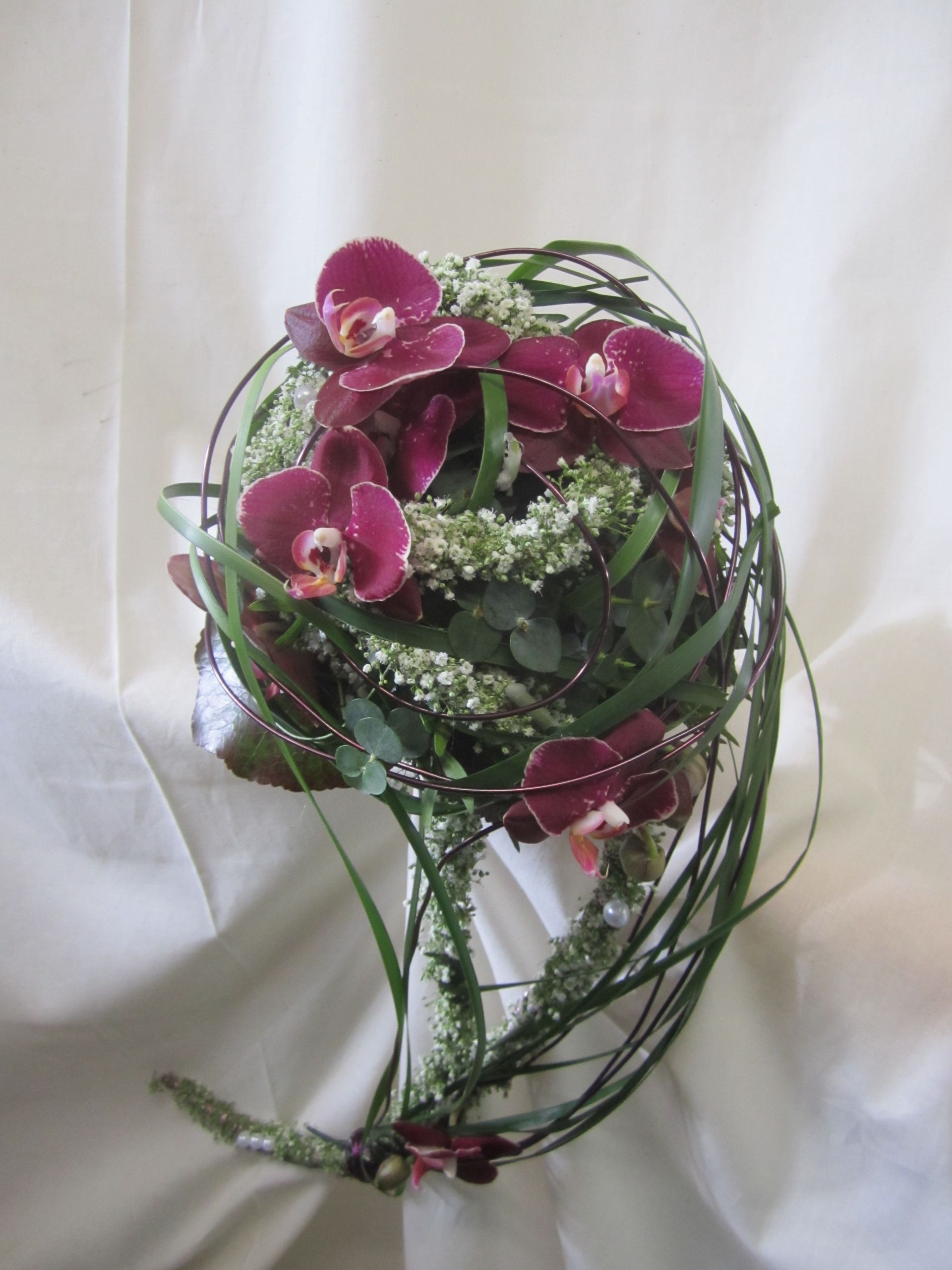 Strauß aus tiefmagentafarbenen Orchideen und weißen Blumen, mit grünen Strängen verwoben.