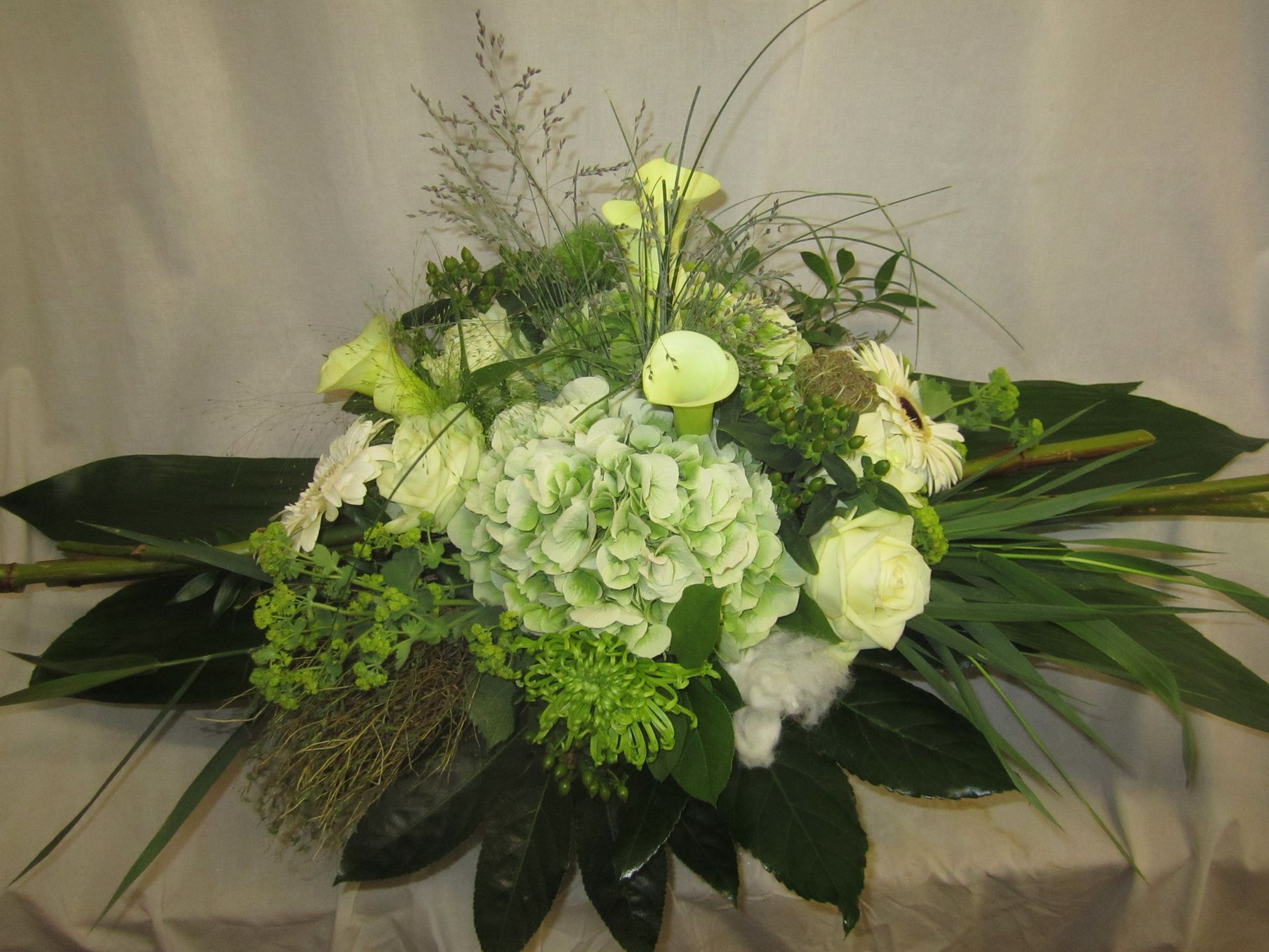 Blumenarrangement mit weißen und grünen Blüten, darunter Rosen und Hortensien, auf einem Tisch.