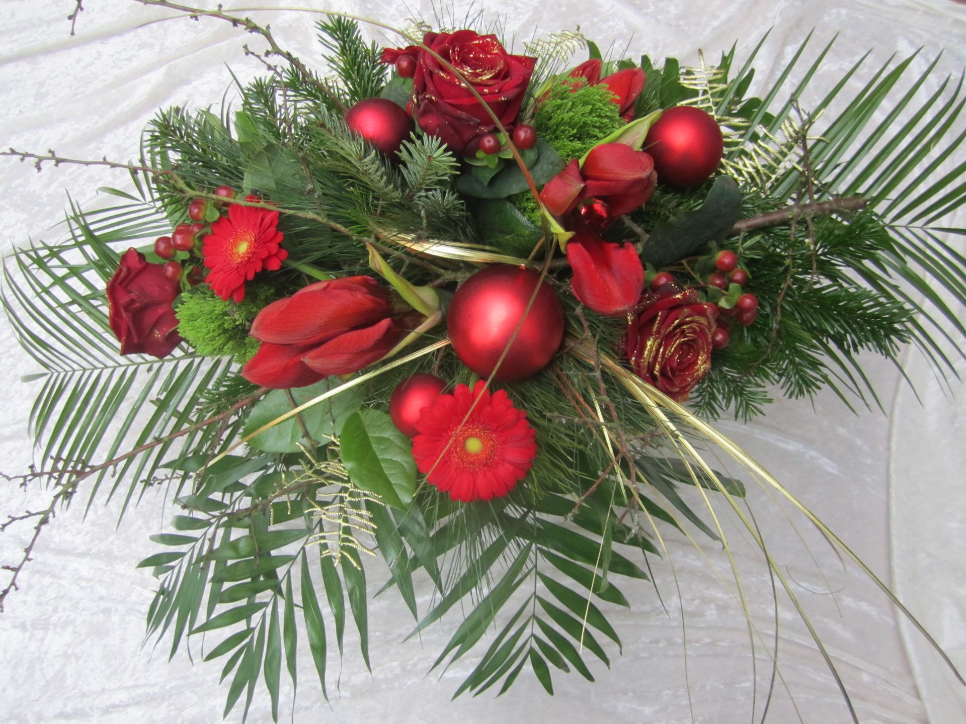 Festliches Blumenarrangement mit roten Rosen, Ornamenten und Grünpflanzen.