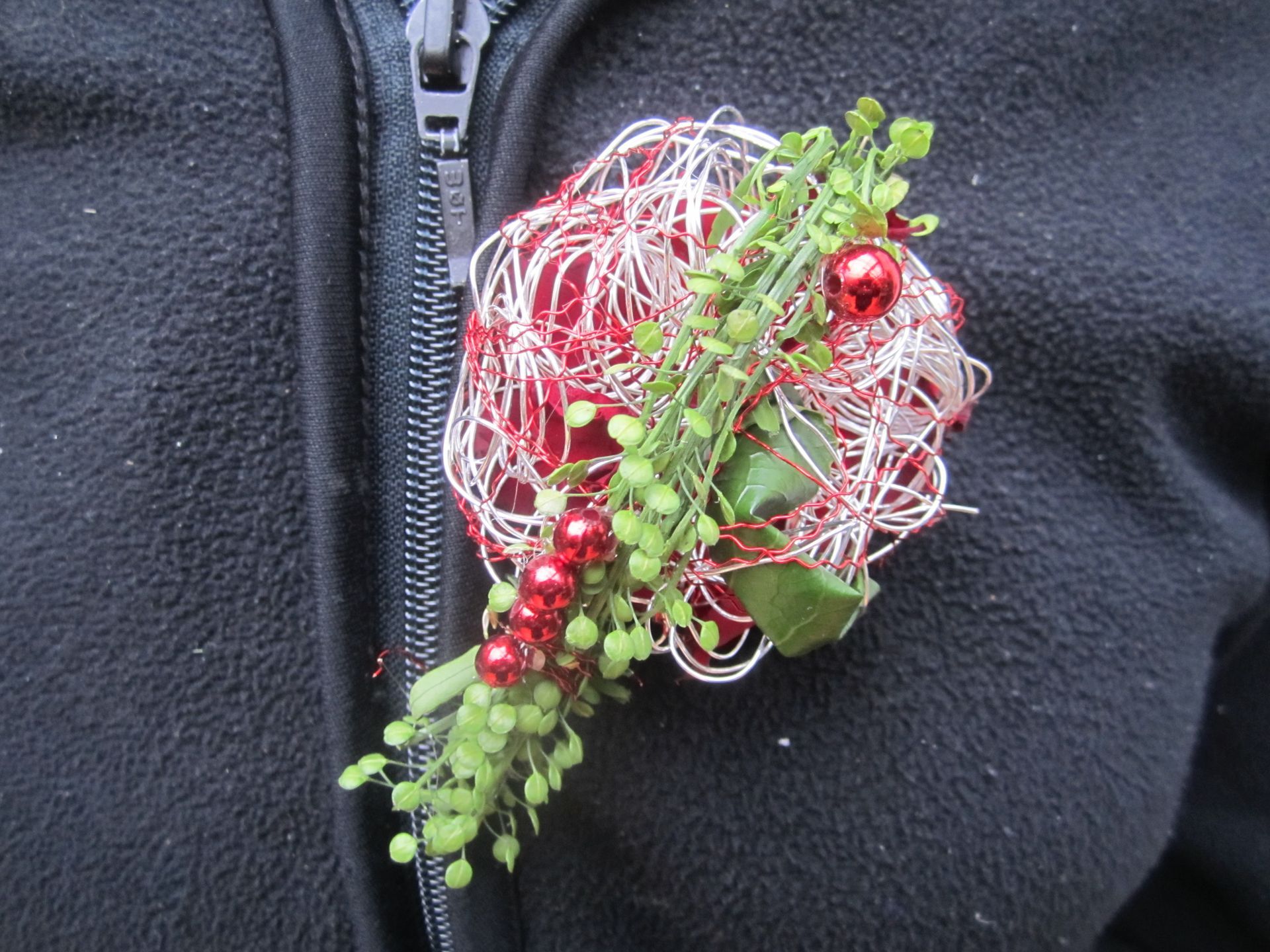 Weihnachtsblumen-Anstecker aus rotem und silbernem Draht, an einer schwarzen Jacke befestigt.