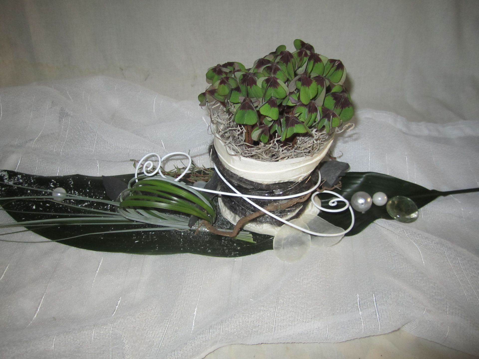 Kleines Blumenarrangement mit grünen und violetten Blättern, Perlen und weißem Draht auf weißem Stoff.