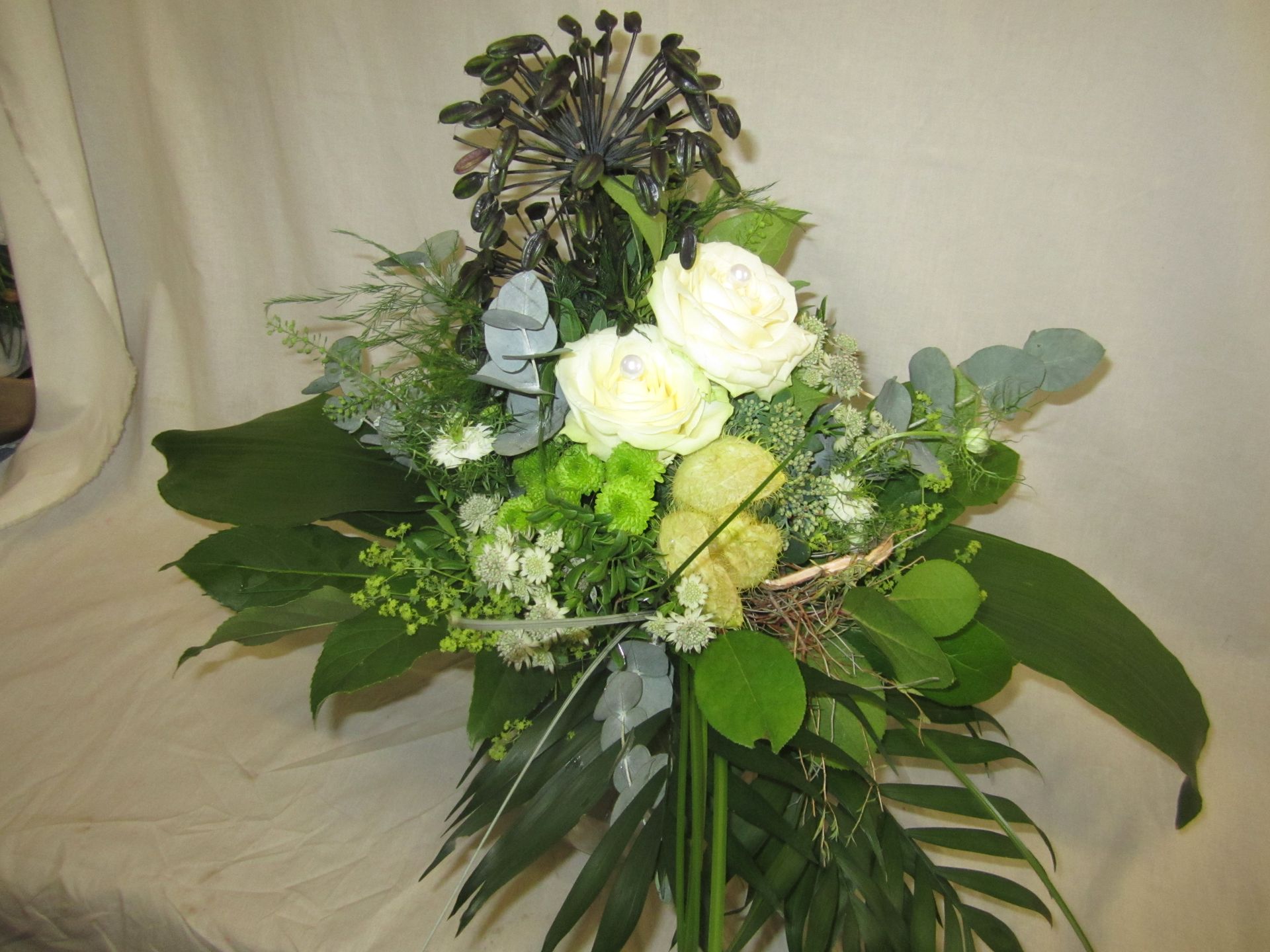 Blumenarrangement mit weißen Rosen, grünem Laub und dunklen Samenkapseln.