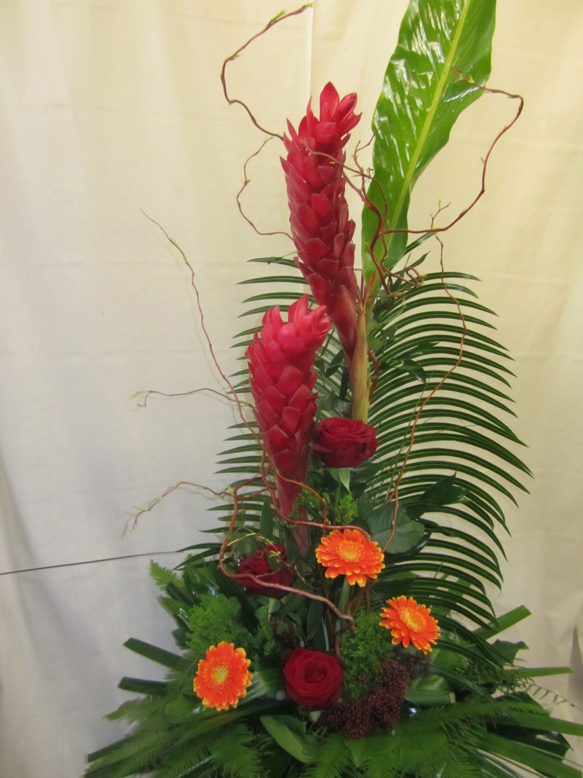 Blumenarrangement mit rotem Ingwer, orangefarbenen Gerbera-Gänseblümchen und Palmblättern.