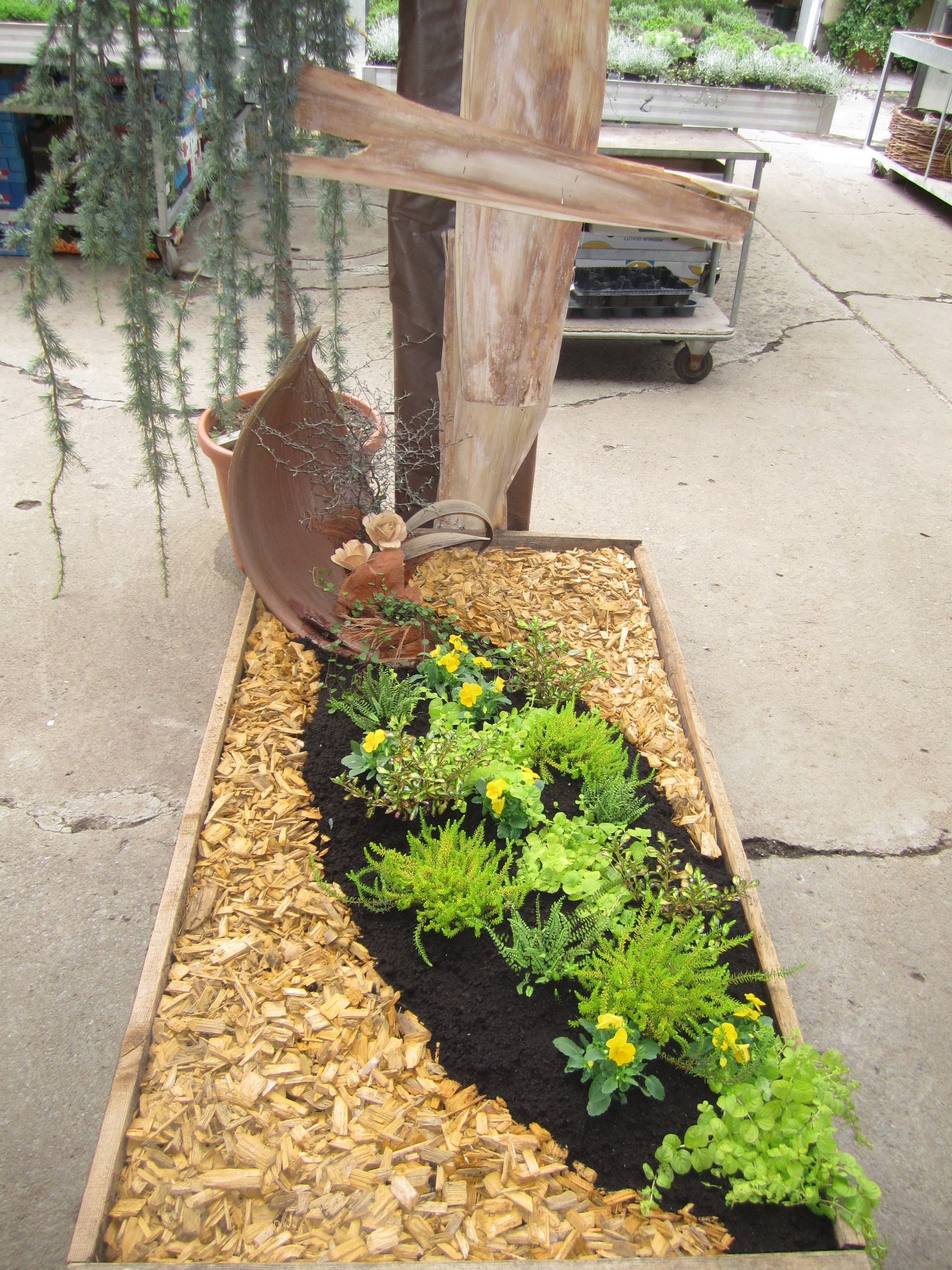 Pflanzkübel aus Holz mit dekorativen Pflanzen, Holzspänen und einem rustikalen Wasserspiel.