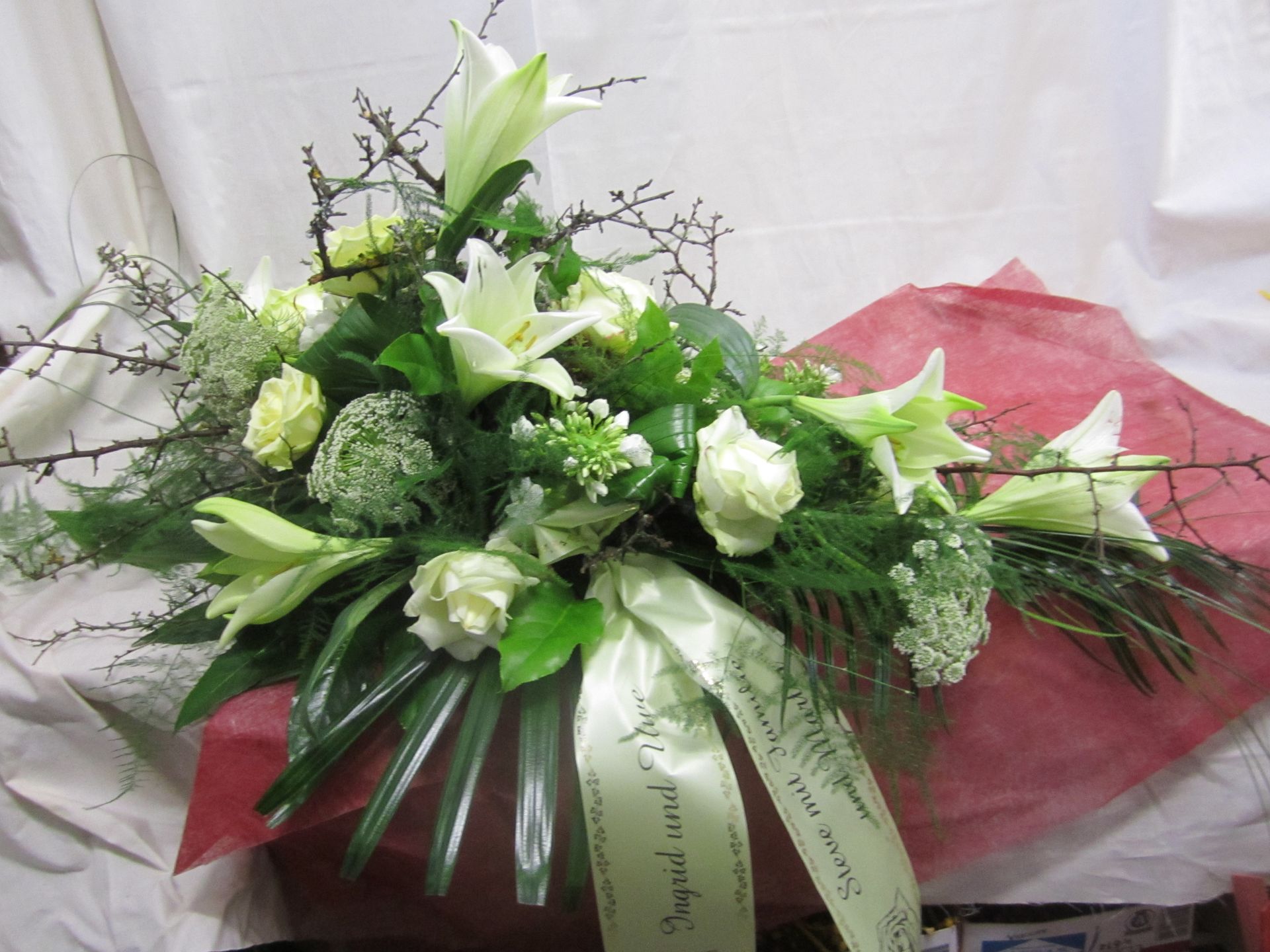 Weiße Lilien und Rosen in einem Blumenarrangement mit einem grünen Band auf rotem Papier.