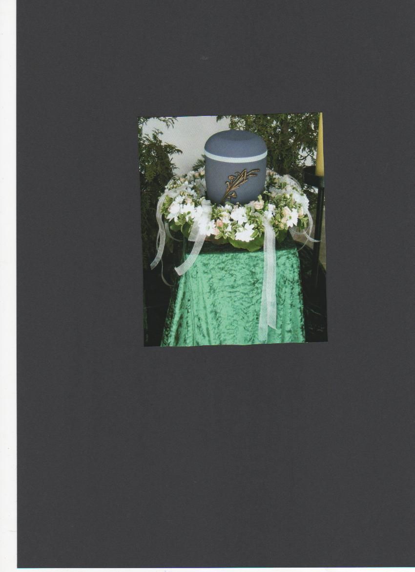 Urne auf einem grün gedeckten Tisch, umgeben von einem weißen Blumenkranz.