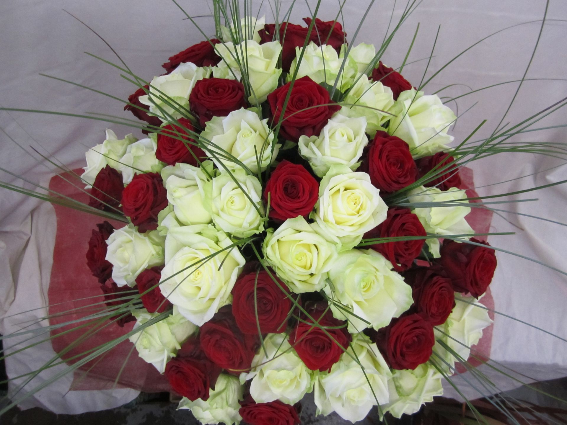 Strauß roter und weißer Rosen mit grünen Zweigen.