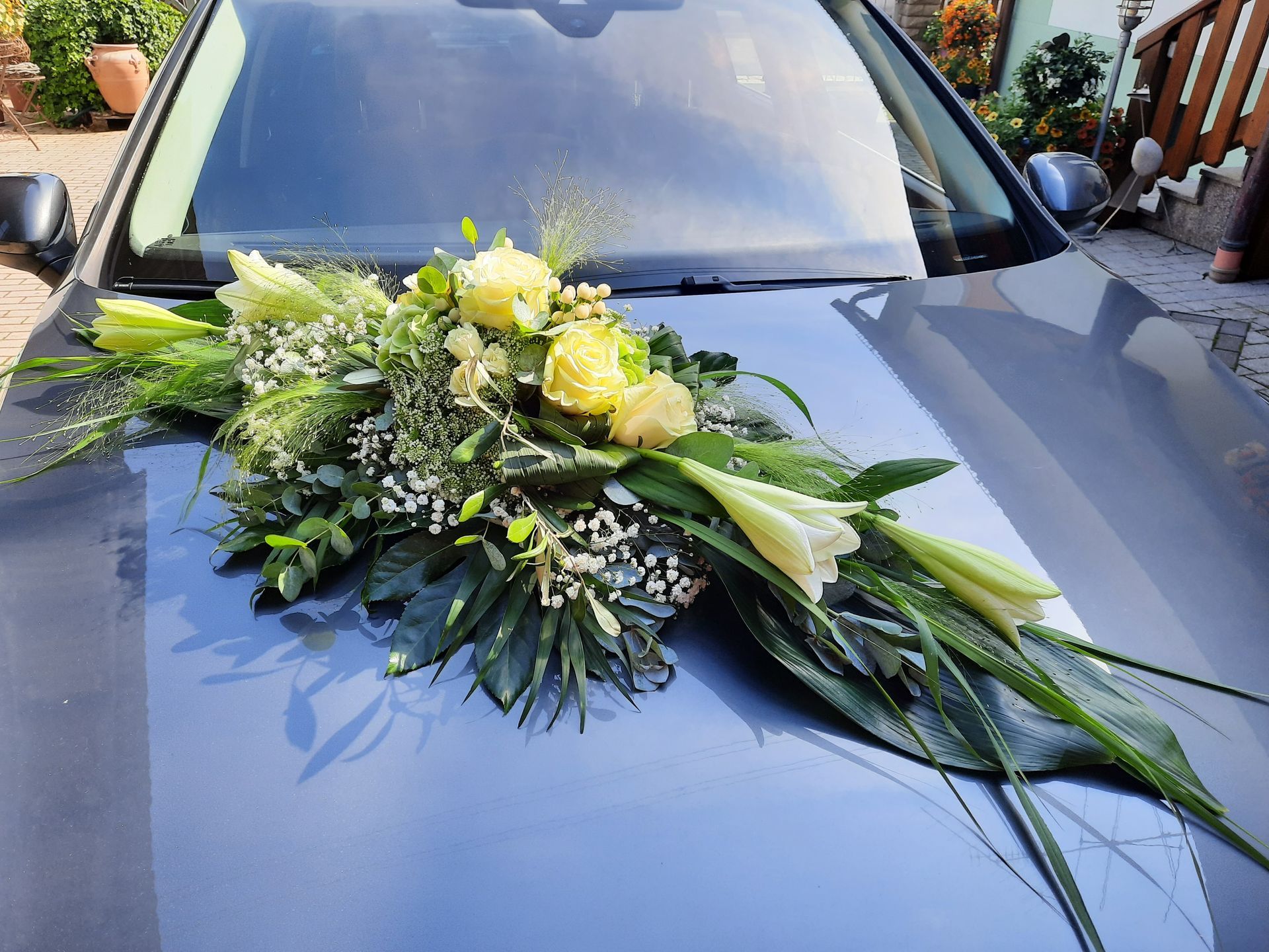 Hochzeitsauto, geschmückt mit gelben Rosen, Lilien und Grünpflanzen auf einer grauen Motorhaube.