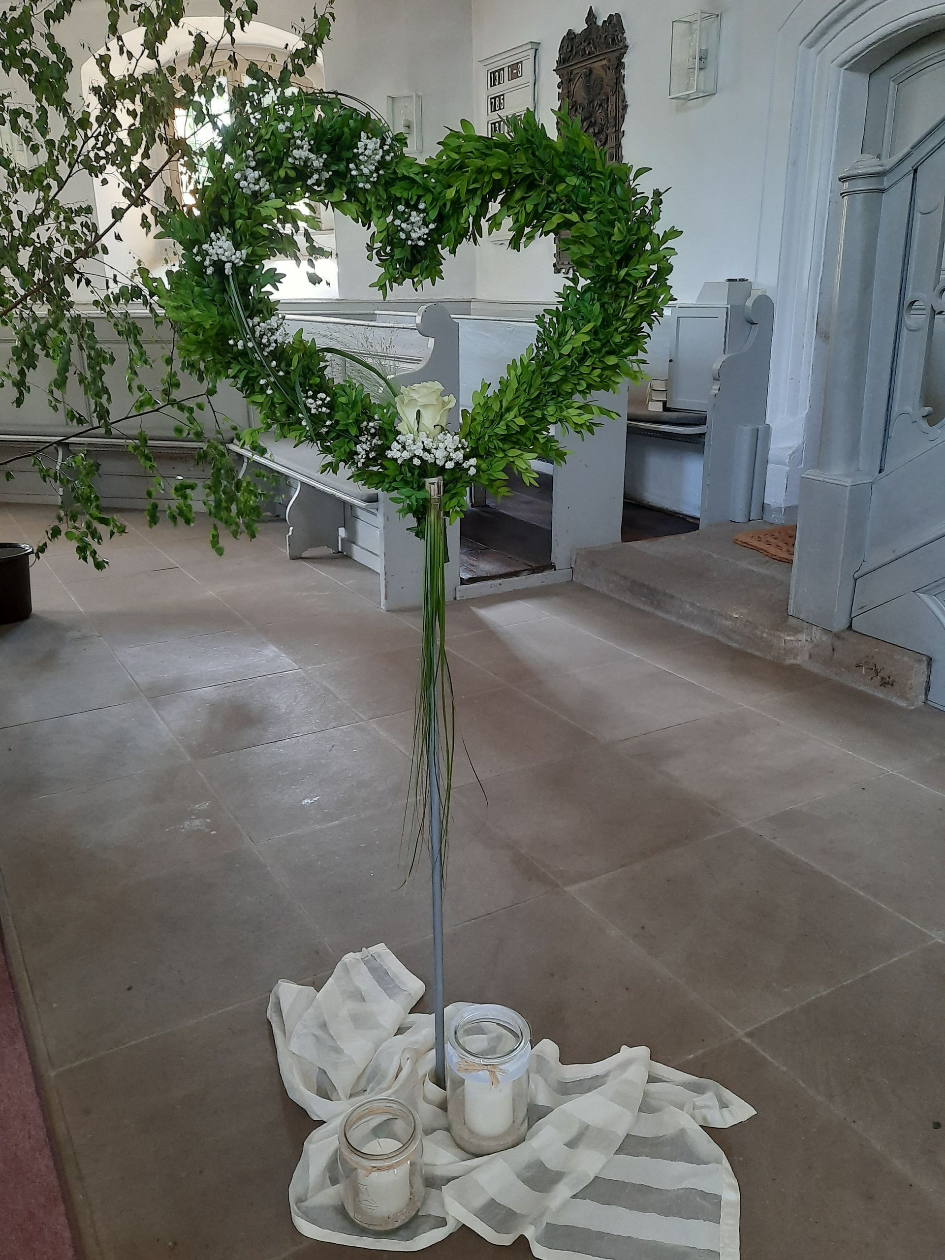 Herzförmiges grünes Tafelaufsatz mit Kerzen in einer Kirche.