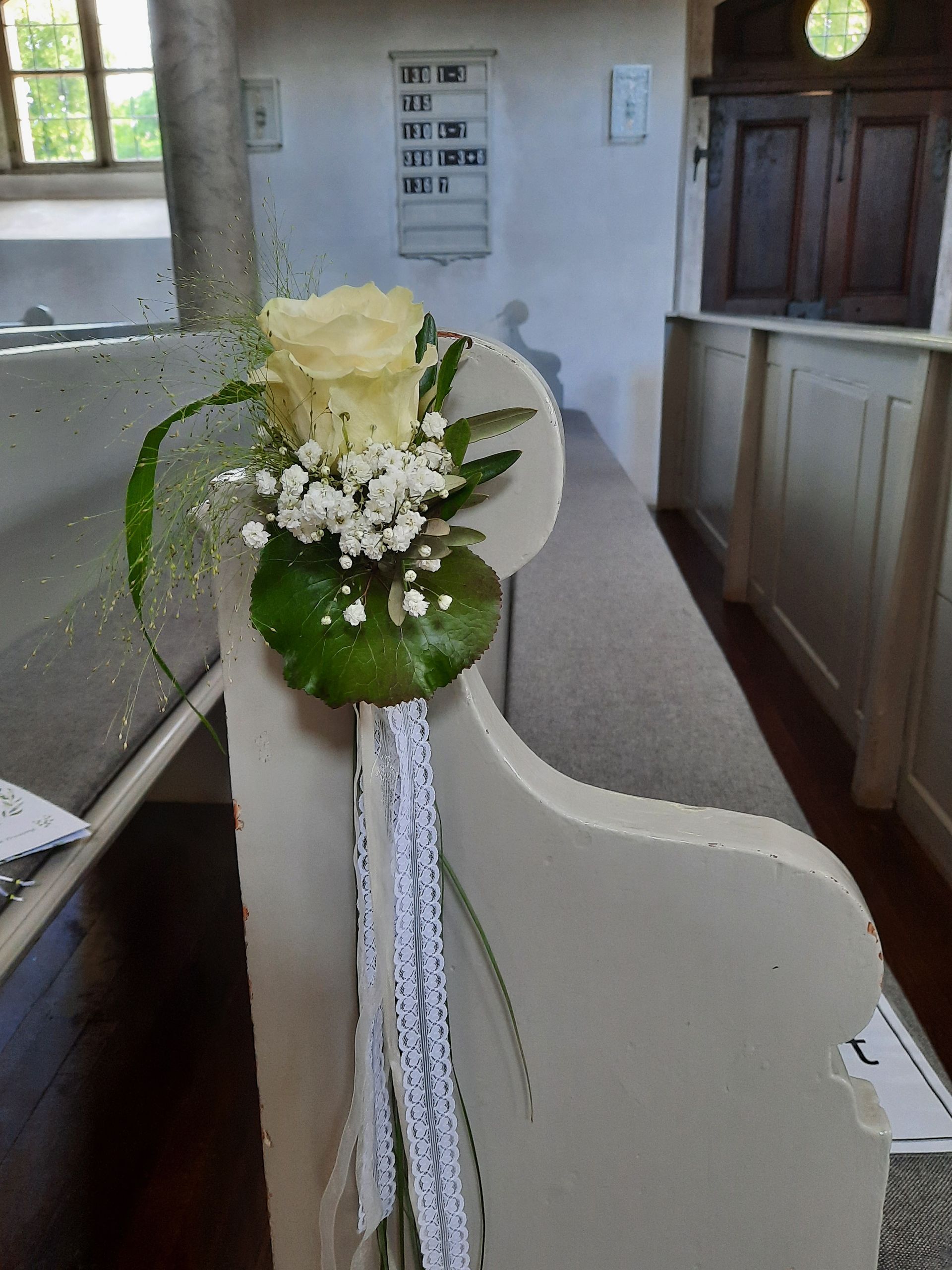 Weiße Kirchenbank mit Rosen- und Blumenschmuck.