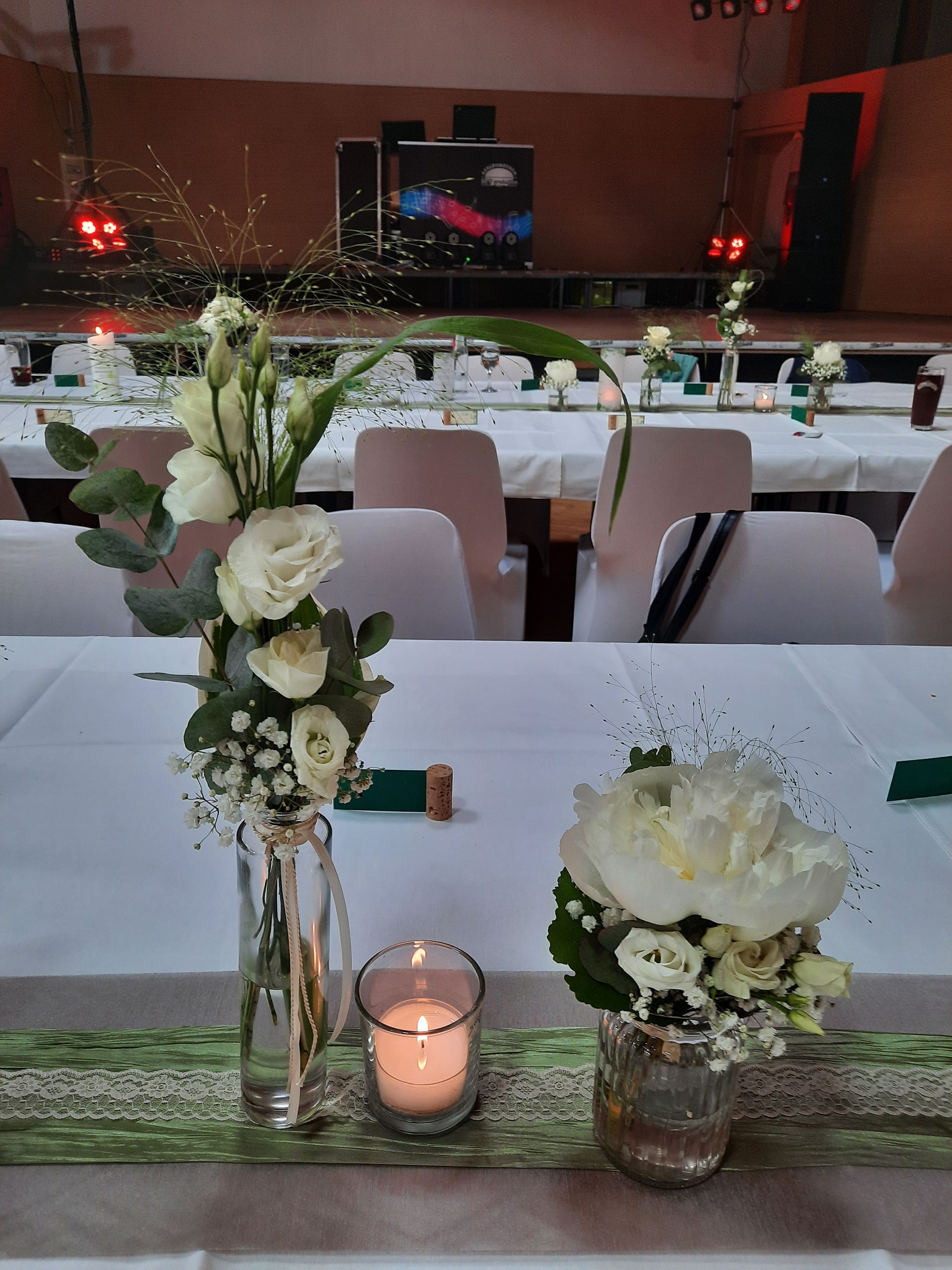 Hochzeitsempfangstisch mit Blumengestecken, Kerzen und weißer Tischwäsche.