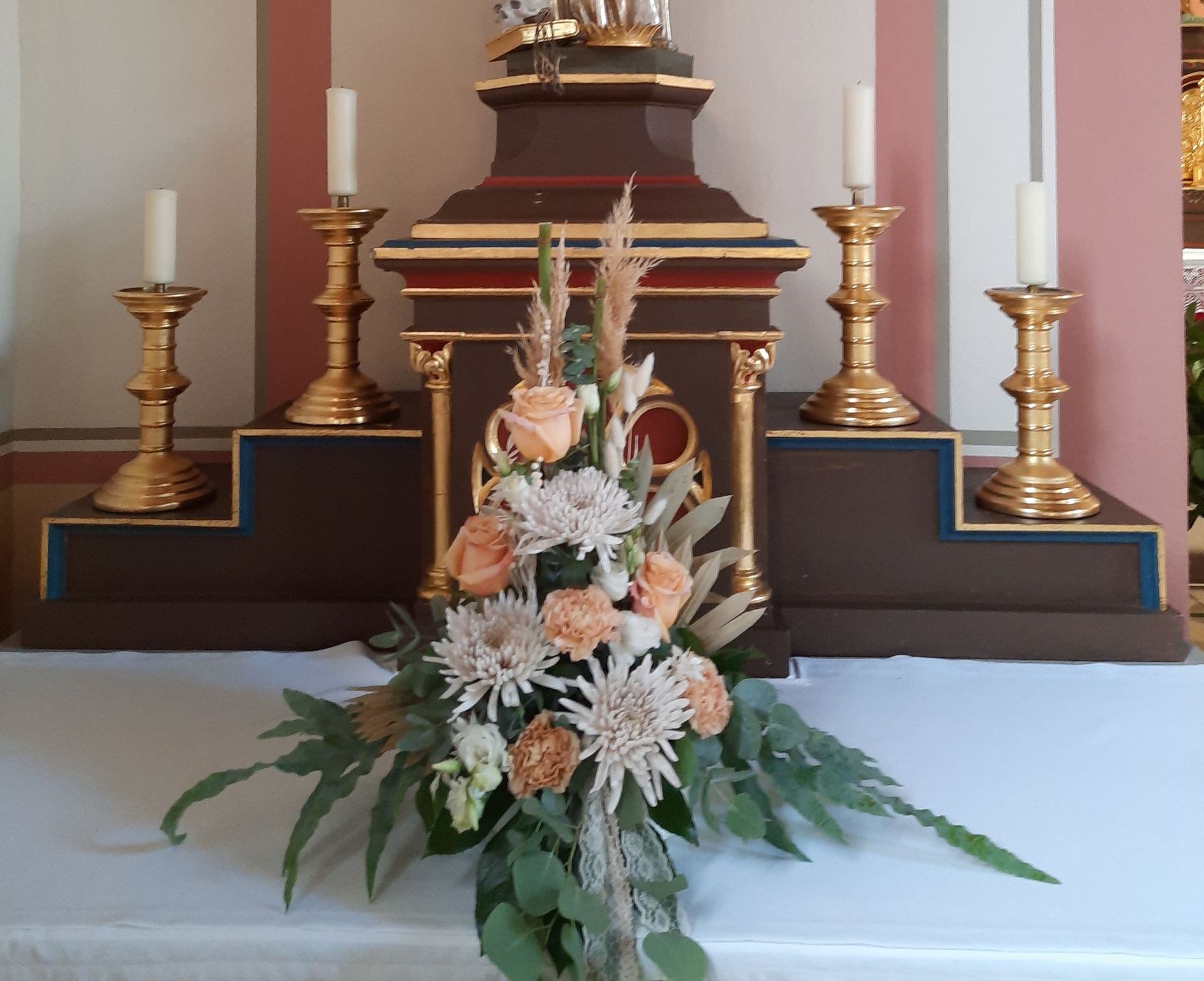 Blumenarrangement auf einer weißen Fläche vor einem Kirchenaltar mit Kerzen.