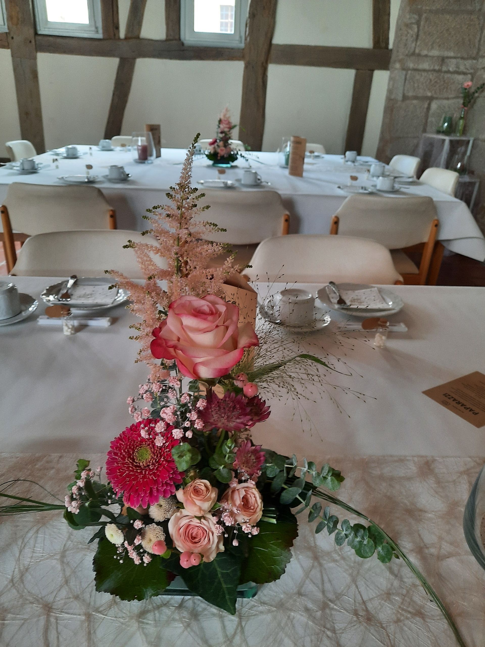 Blumendekoration auf einem langen, für eine Versammlung gedeckten Tisch mit Stühlen und rustikalem Interieur.