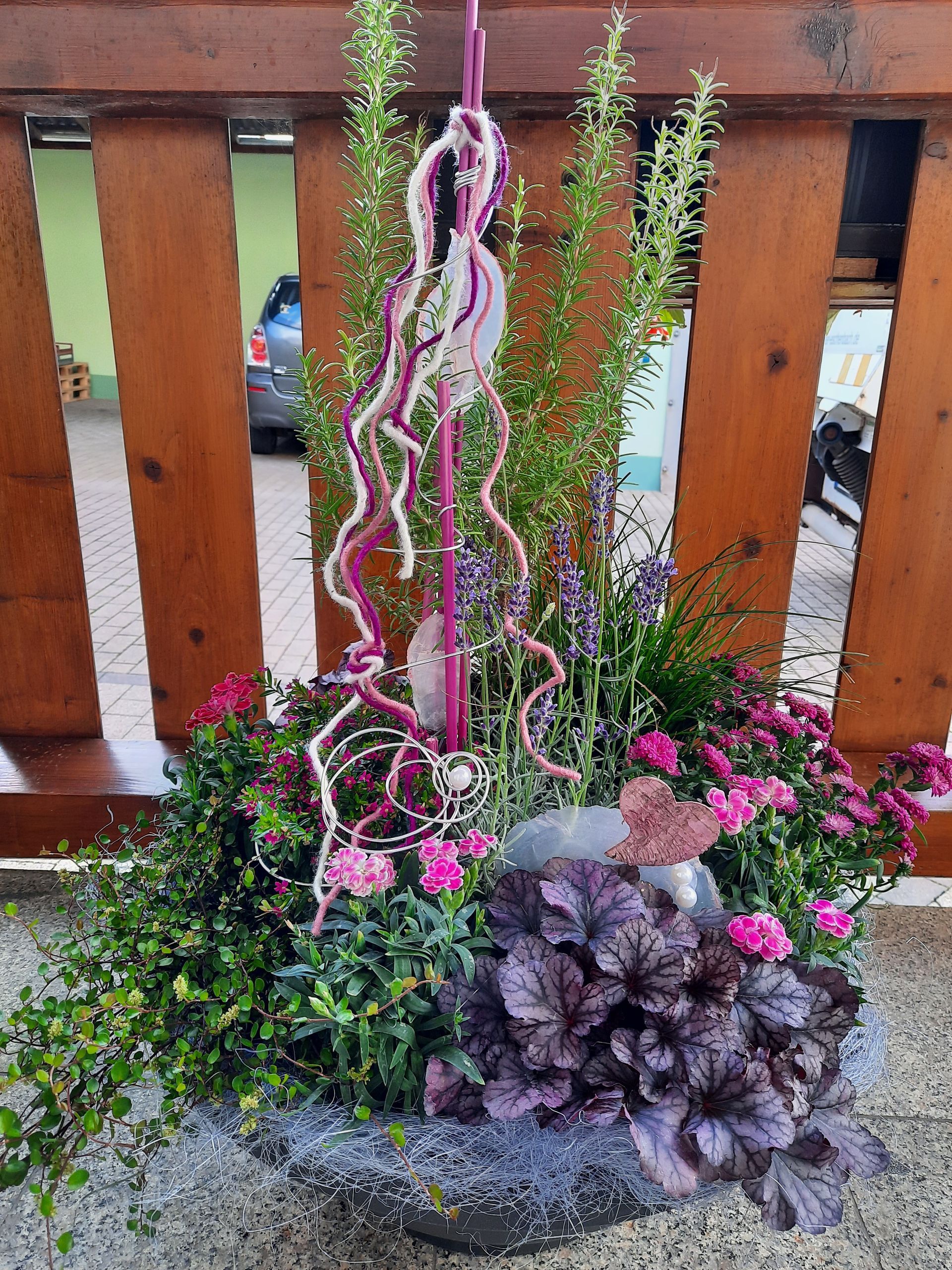 Blumenarrangement mit violetten und rosa Blüten, Grünpflanzen und dekorativen Akzenten.