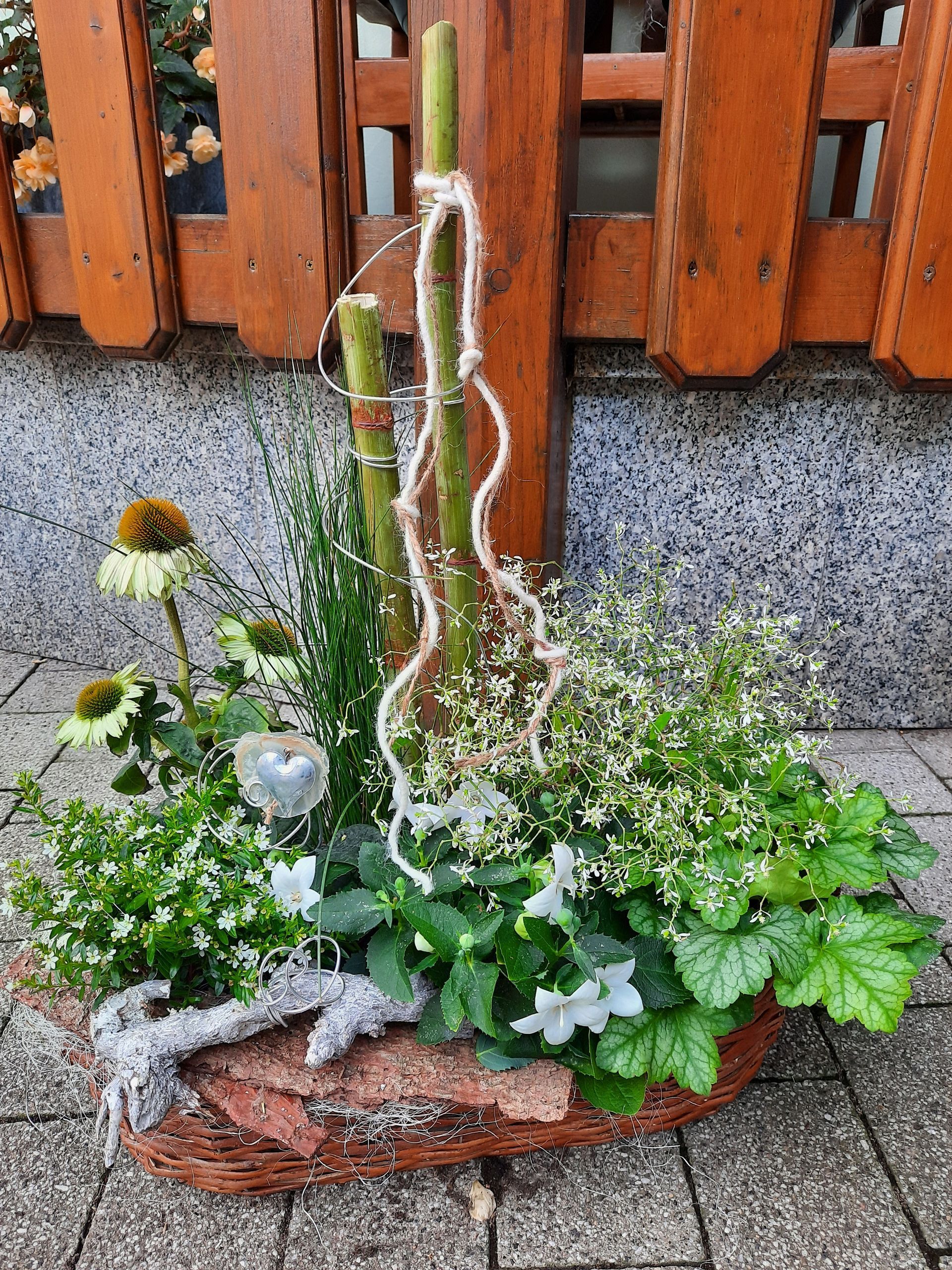 Blumenarrangement in einem Korb mit grünen Blättern, weißen Blüten und hohem Bambus.