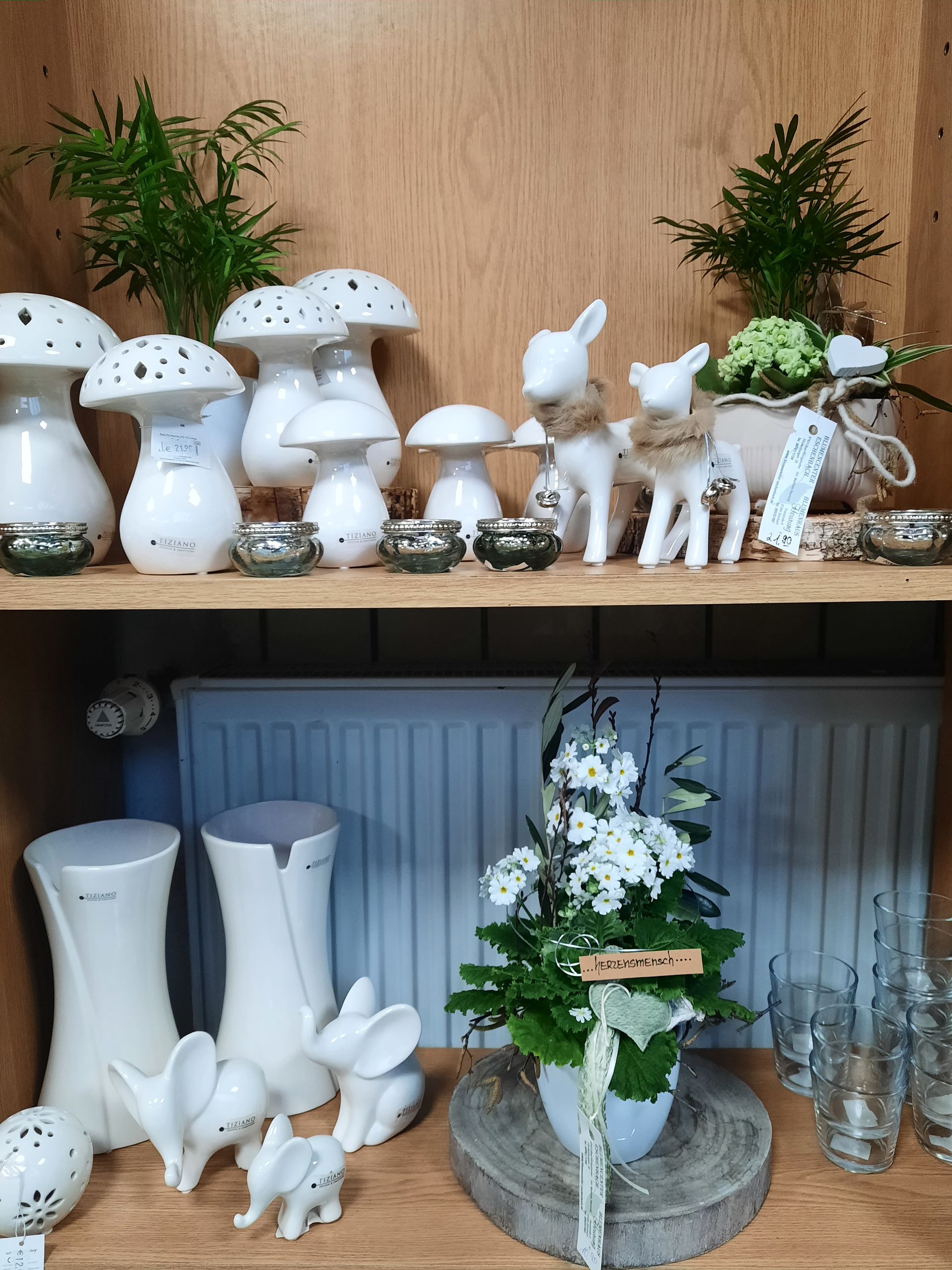 Regalpräsentation: weiße Pilz- und Kaninchenfiguren, grüne Pflanzen, Votivkerzen aus Glas.