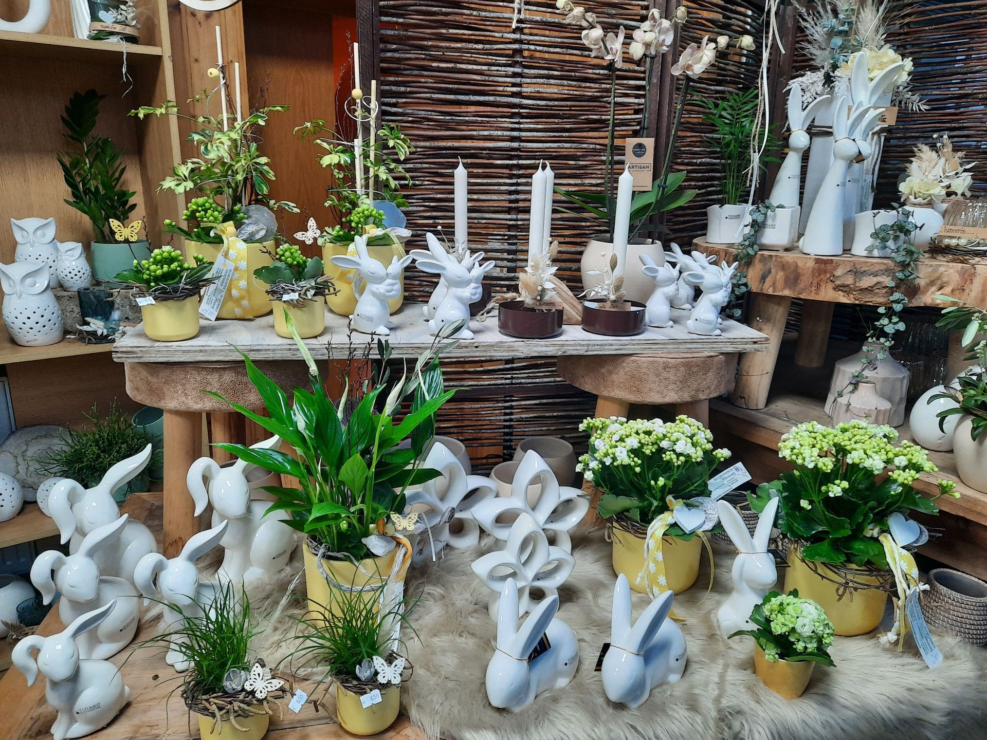 Osterdekorationen mit weißen Keramikhasen, Topfpflanzen, Kerzen und Blumen auf rustikalen Holztischen.