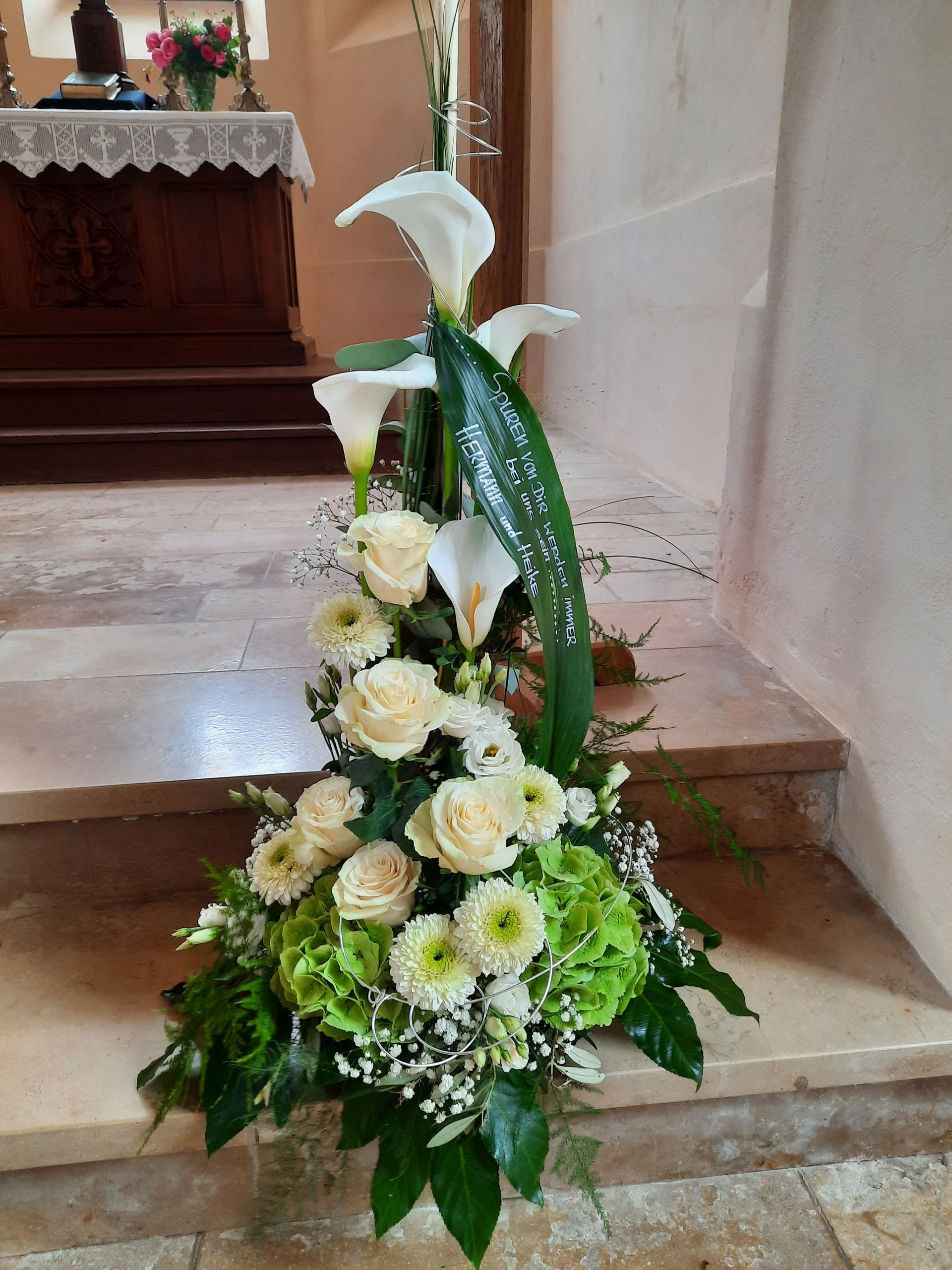 Blumenarrangement mit weißen Calla-Lilien und Rosen auf den Kirchenstufen.
