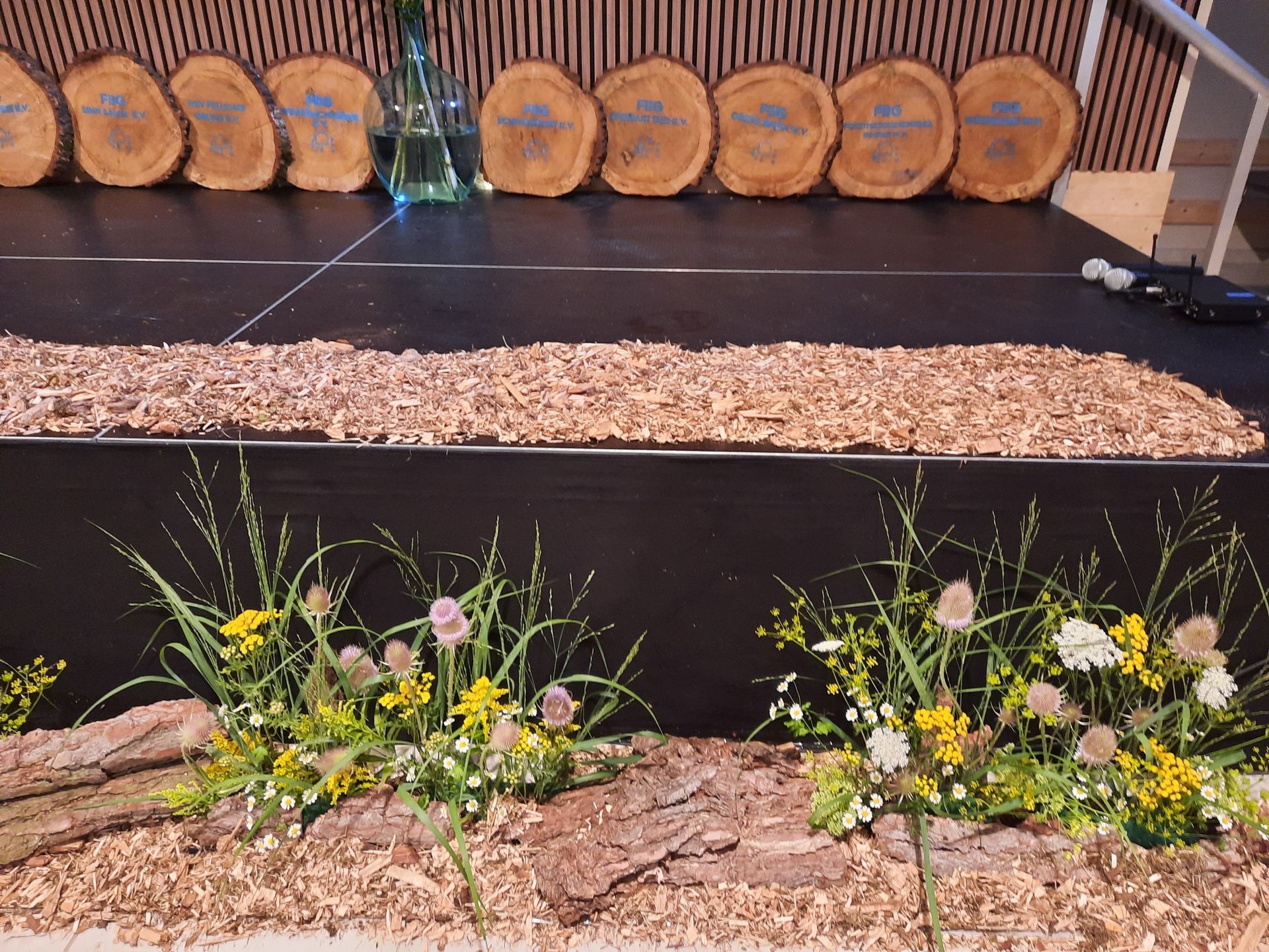 Bühne dekoriert mit Holzscheiben, Rinde, Holzspänen und Blumen.