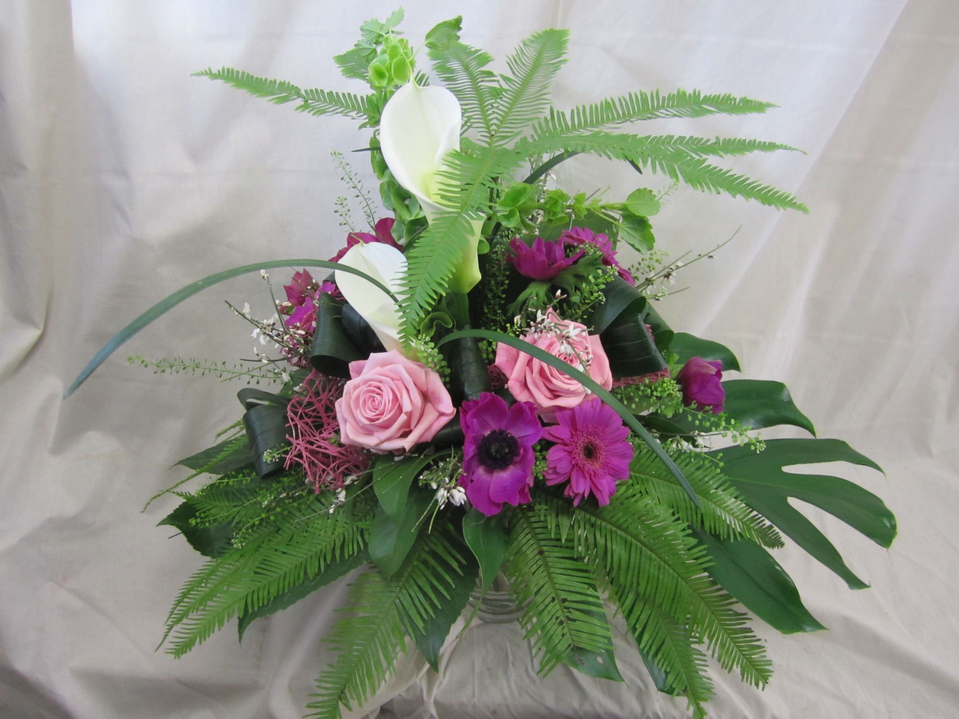 Blumenarrangement: rosa Rosen, Callas, grüne Farne und violette Blumen.