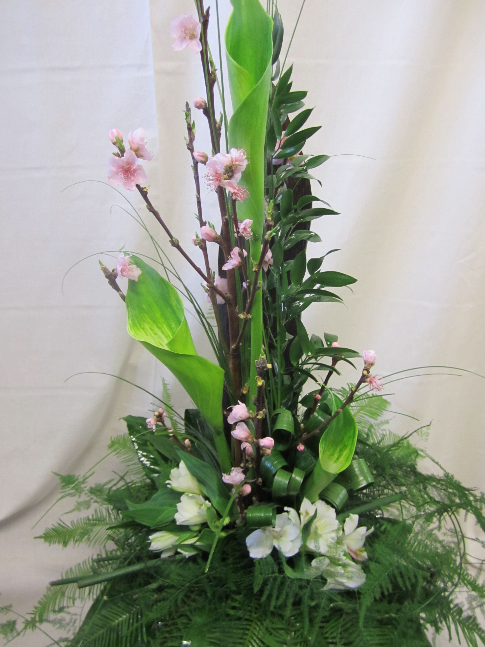 Blumenarrangement: grüne Blätter, Pfirsichblüten, weiße Blumen, hohe, vertikale Anordnung.