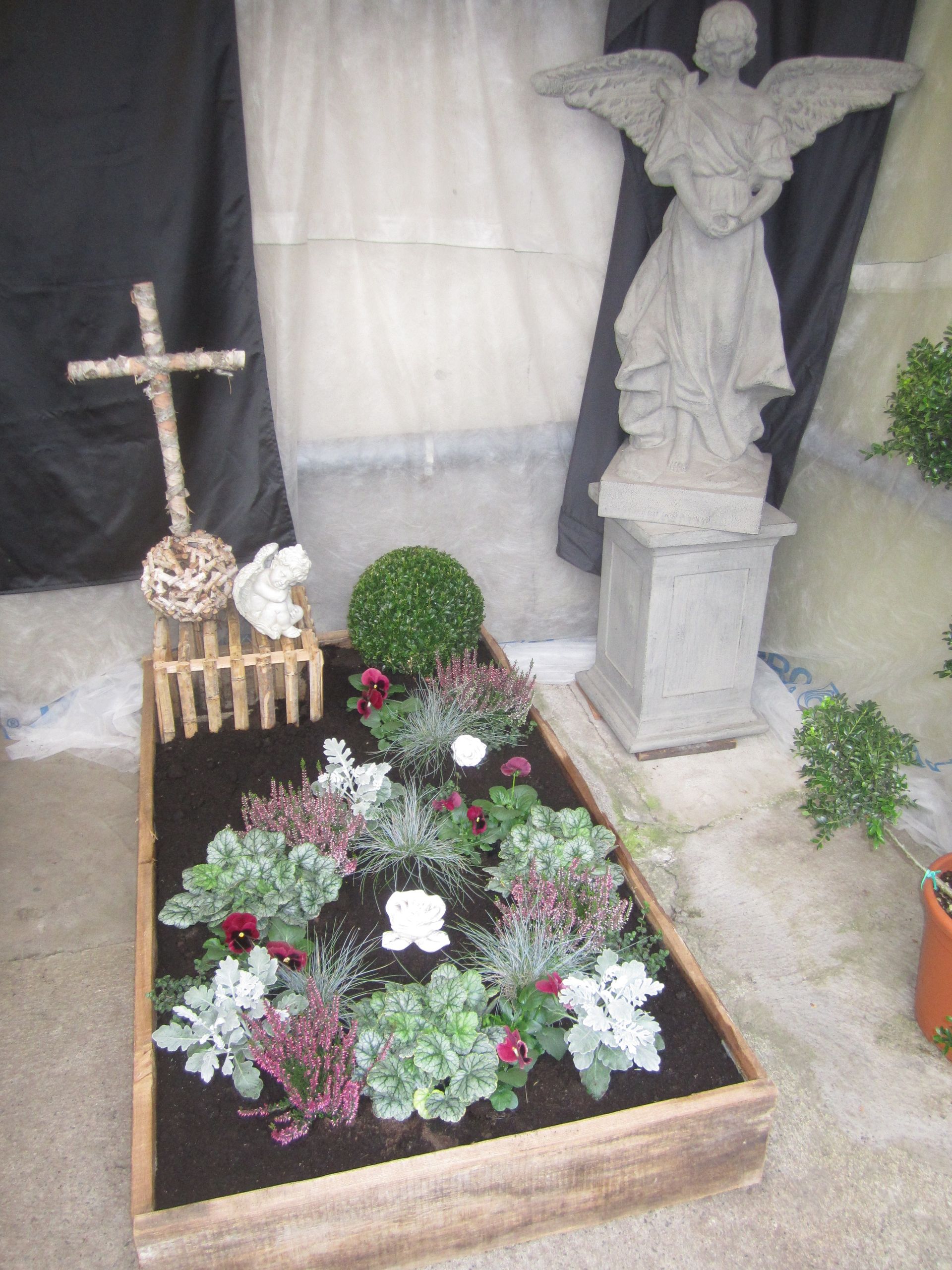 Grab mit Kreuz, Engelsstatue und Blumen, möglicherweise als Gedenkstätte oder Dekoration.