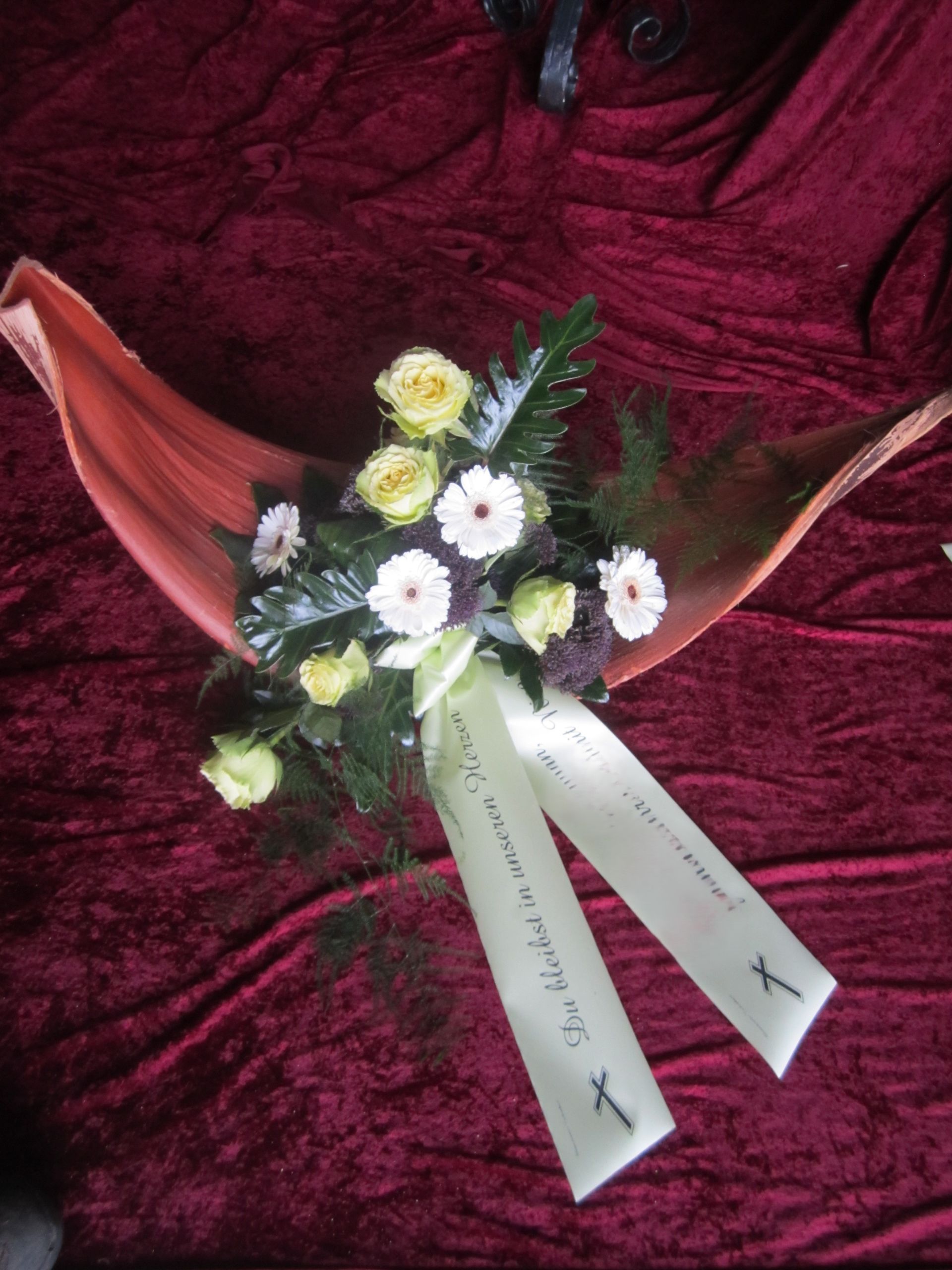 Blumenstrauß aus weißen Gänseblümchen und gelben Rosen mit Schleife vor kastanienbraunem Hintergrund.