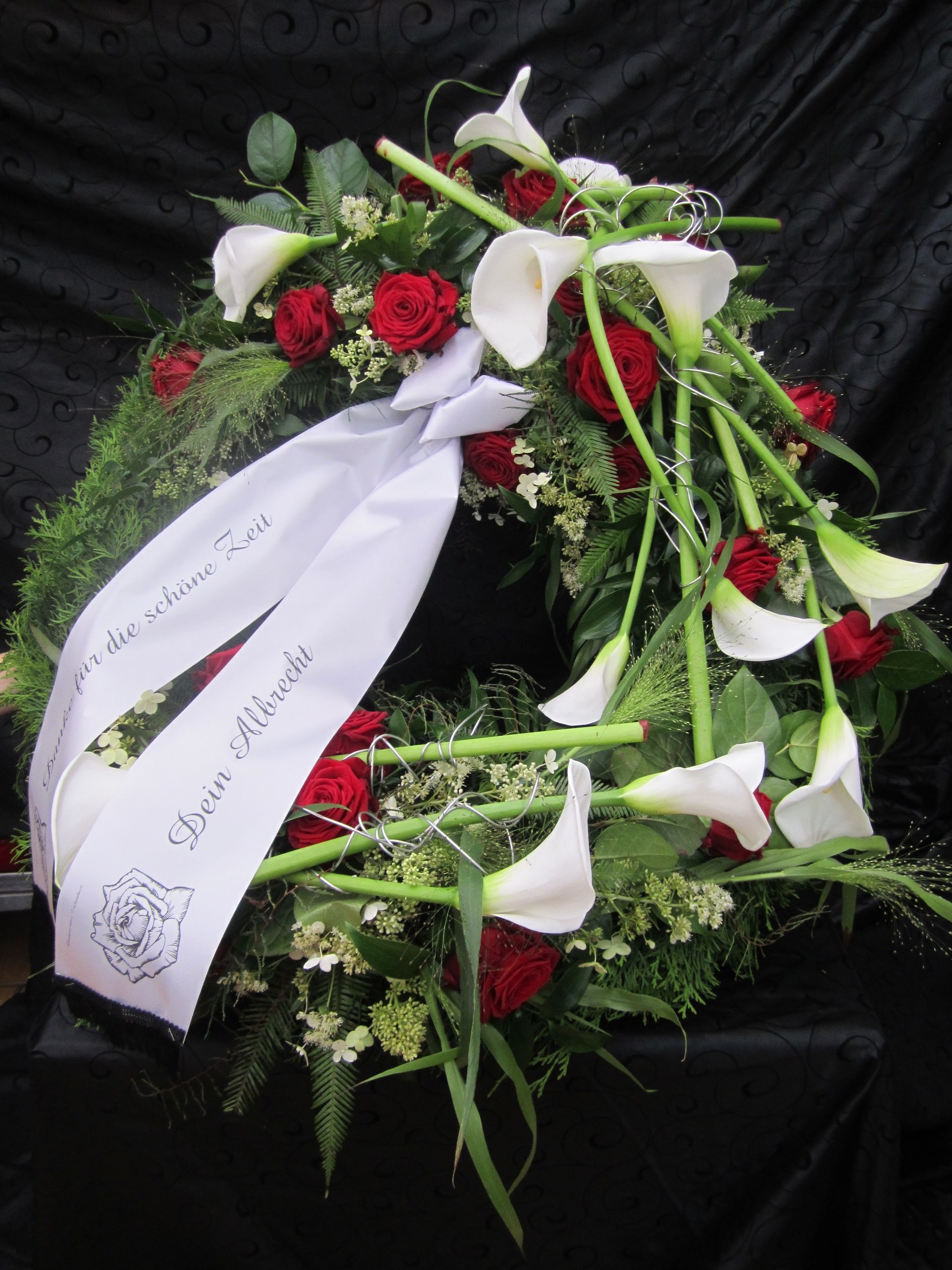 Trauerkranz mit weißen Calla-Lilien, roten Rosen und weißem Band.