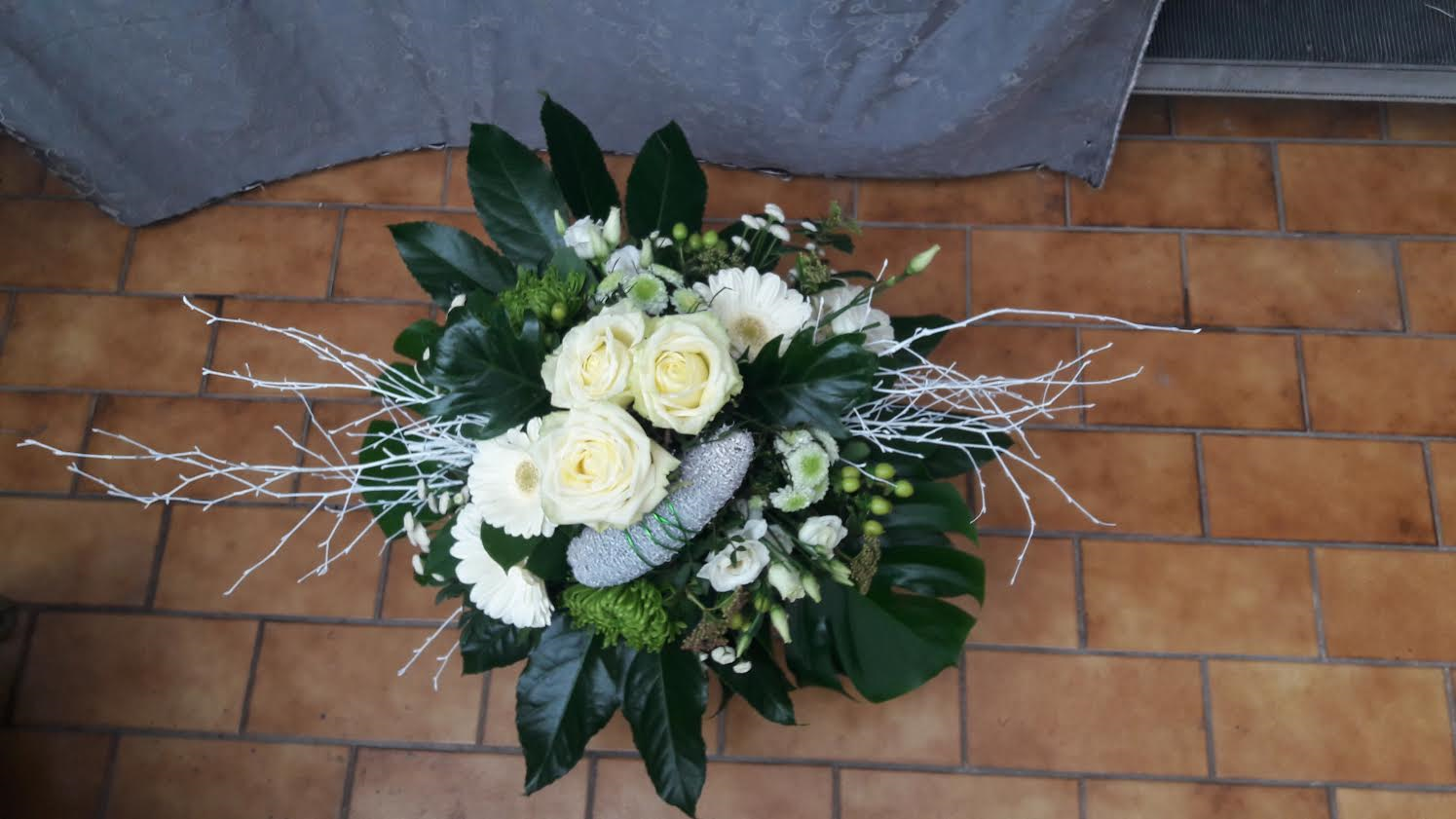 Weißes und grünes Blumenarrangement mit Rosen vor einer Ziegelwand.