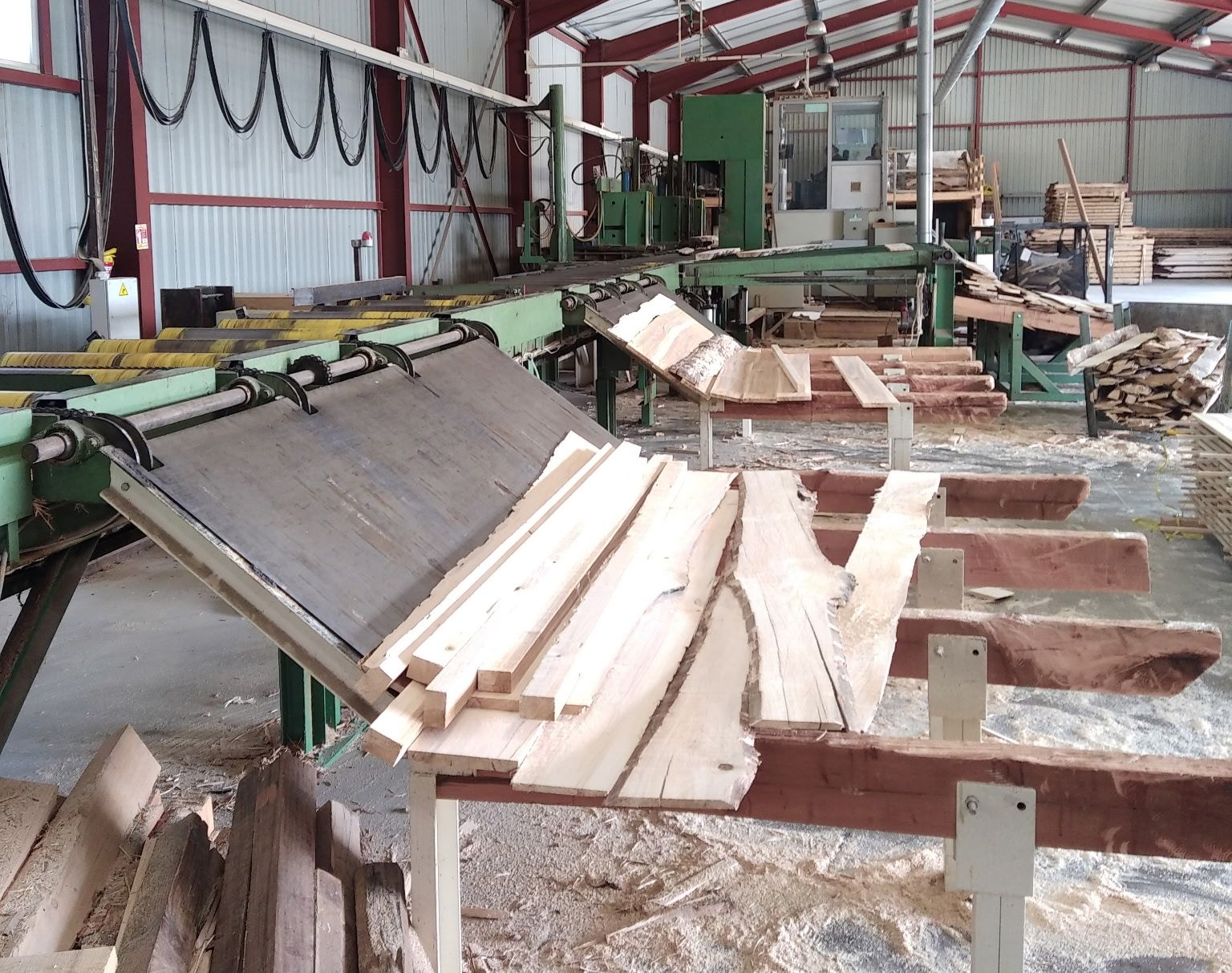 Poste de tri et de manutention du bois dans une scierie, avec des planches fraîchement sciées disposées sur un convoyeur industriel.