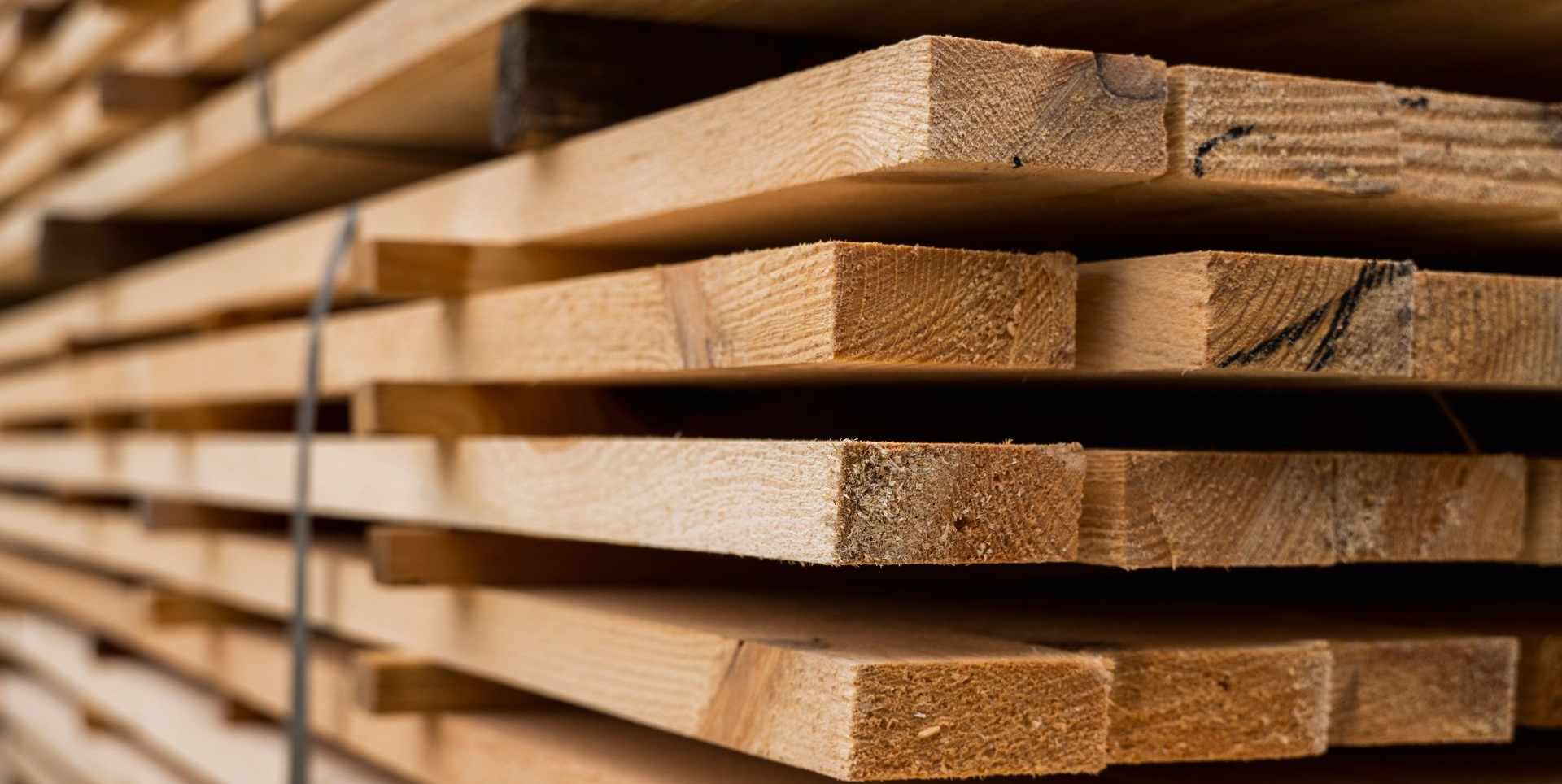 Pile de planches de bois, de tailles et de couleurs variées, probablement destinées à la construction ou à la menuiserie.