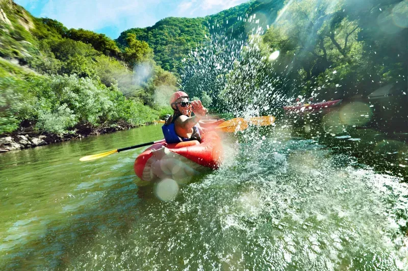 Person in red kayak on river, water splashing, green foliage in background.