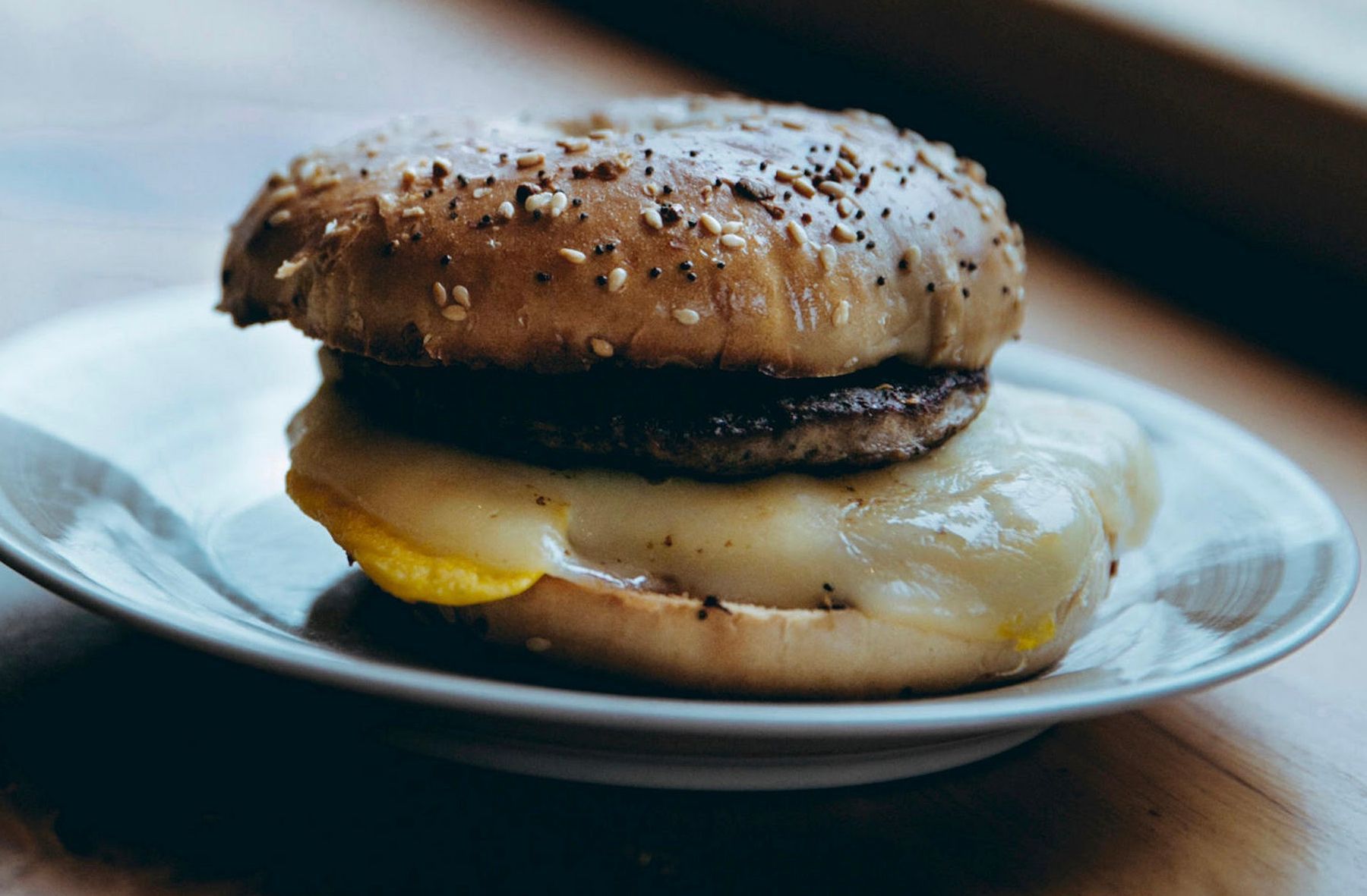 Breakfast sandwich with egg, cheese, and sausage on a bagel, served on a plate.