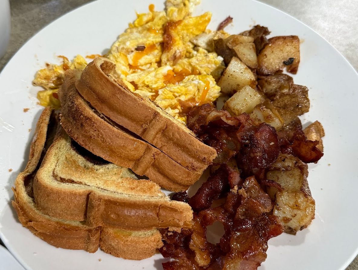Breakfast plate with scrambled eggs, toast, potatoes, and bacon.