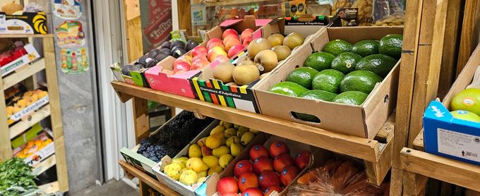 Exhibición de frutas en un mercado, con diversas frutas coloridas en cajas en estantes de madera.