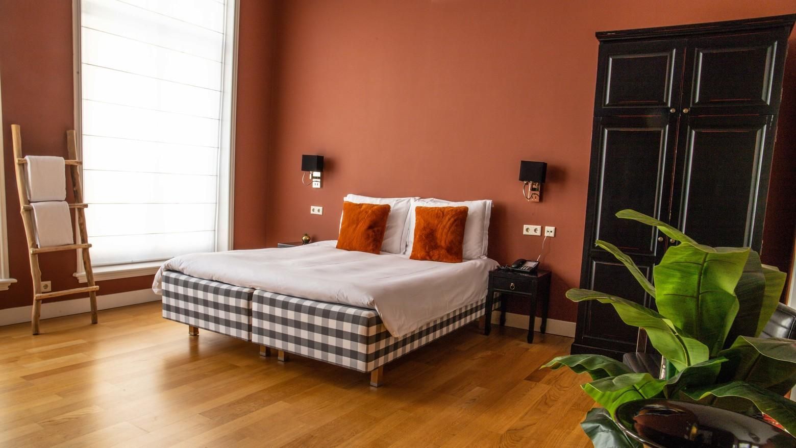 Ruime slaapkamer met een bed, terracotta muren, houten vloer en een potplant naast een kledingkast.