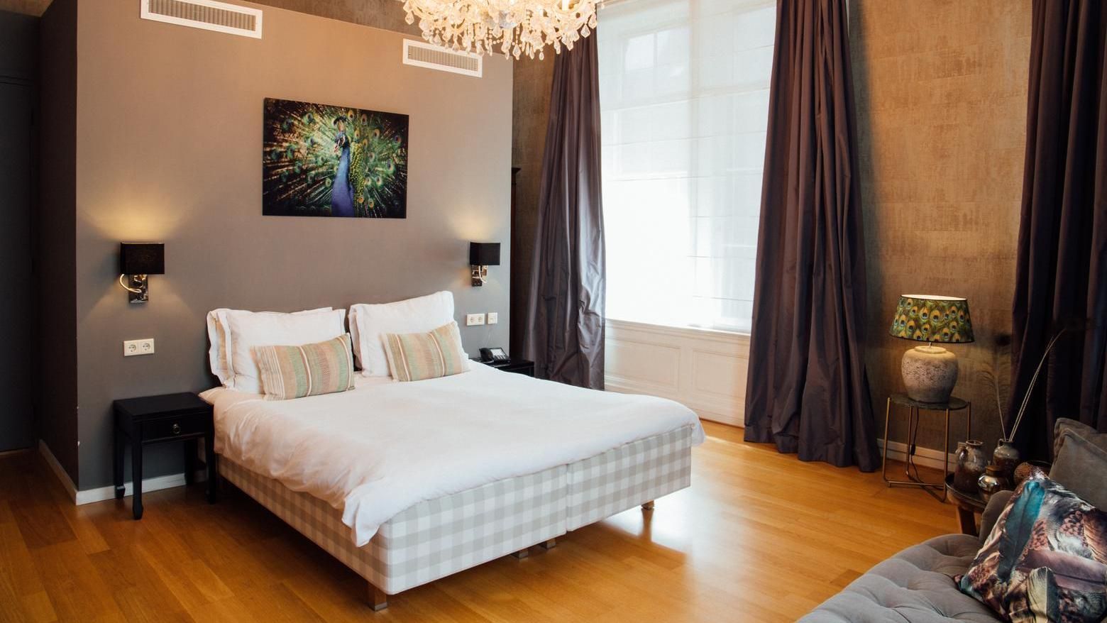 Moderne slaapkamer met een wit bed, donkere gordijnen, houten vloer en een groot raam met veel natuurlijk licht.