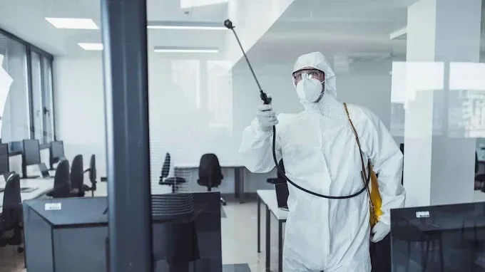 Une personne en combinaison de protection pulvérise du désinfectant dans un bureau.