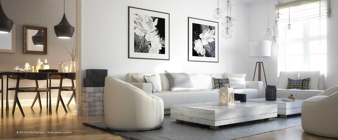 heller und modern eingerichteter Wohnbereich mit hellem Sofa, zwei Couchtischen und Schwarz-Weiß-Bildern an der Wand