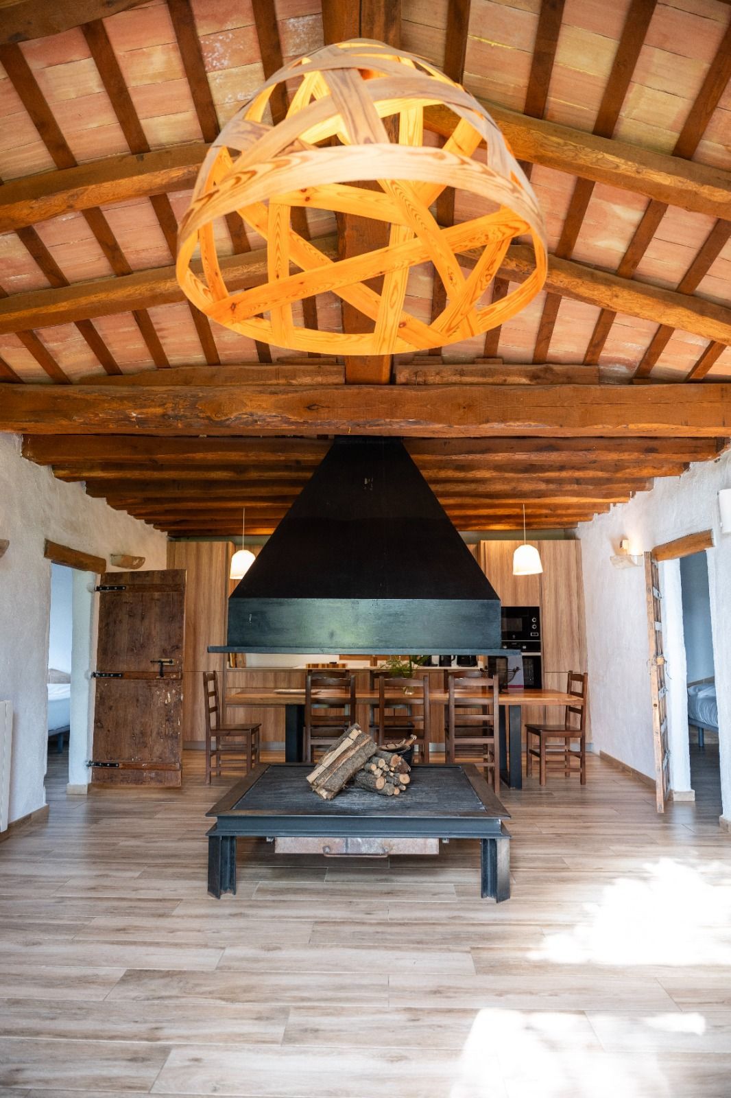 Sala de estar rústica estilo cabaña con vigas a la vista, lámpara colgante de madera y chimenea central.